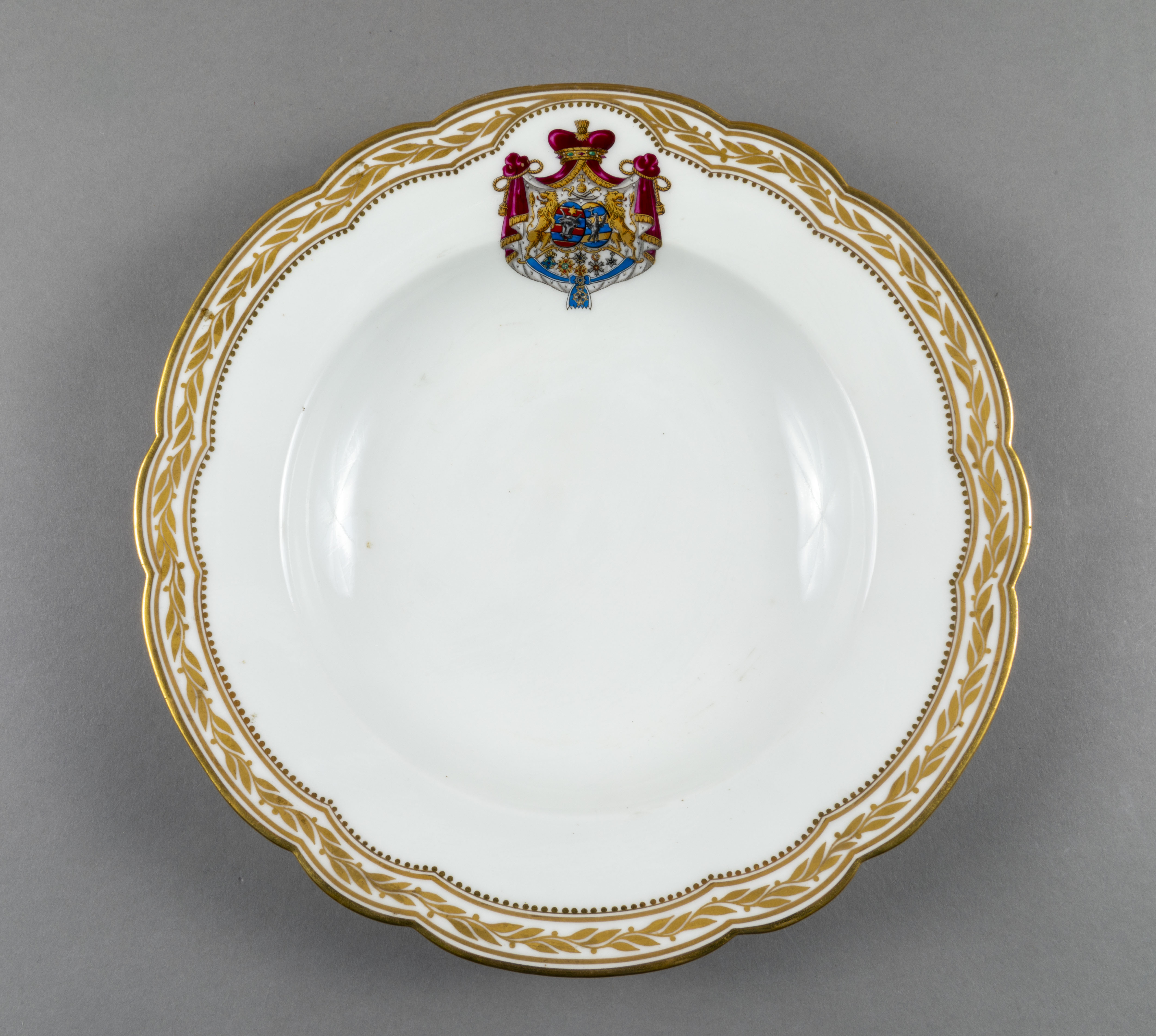 Farfurie adâncă de porțelan de Sevres, realizată din porțelan alb, cu margini treflate, decorate cu frunze de laur pictate, în centrul decorațiilor având blazonul familiei Suțu. Blazonul a fost adesea confundat cu cel al Principatelor Unite, fiind format din: stemele celor două țări românești: prima cea a Moldovei, cea de-a doua cea a Țării Românești, steme plasate pe două scuturi ovale, în fascie, acolate, puțin suprapuse, cea a Moldovei având capul de bour de argint cu stea în șase colțuri de aur, pe un scut cu segmente verticale egale roșii și albastre; cea a Țării Românești având acvila cruciată de argint, cu crucea de aur, scutul având segmente verticale galbene și albastre. Cele două scuturi au ca tenanți doi lei aurii, deasupra armele familiei Suțu – iataganul și sabia, ambele aurii, precum, pe un pavilion de purpură căptușit cu hermină, brodat cu ciucuri de aur și prins într-o coroană cu pietre scumpe. Pe scut, în partea inferioară se află și decorațiile familiei Suțu. Familia Suțu a fost o familie fanariotă grecească, venită în principate în cea de-a doua parte a secolului al XVIII-lea, având trei domni în ambele țări Românești (Alexandru Suțu, Mihai Suțu și Grigore Suțu). Blazonul familiei poate fi admirat inclusiv pe clădirea Palatului Suțu, astăzi Muzeul de Istorie a Municipiului București. Farfuria are marca atelierului Sevres și modelul din anul 1844, precum și seria.