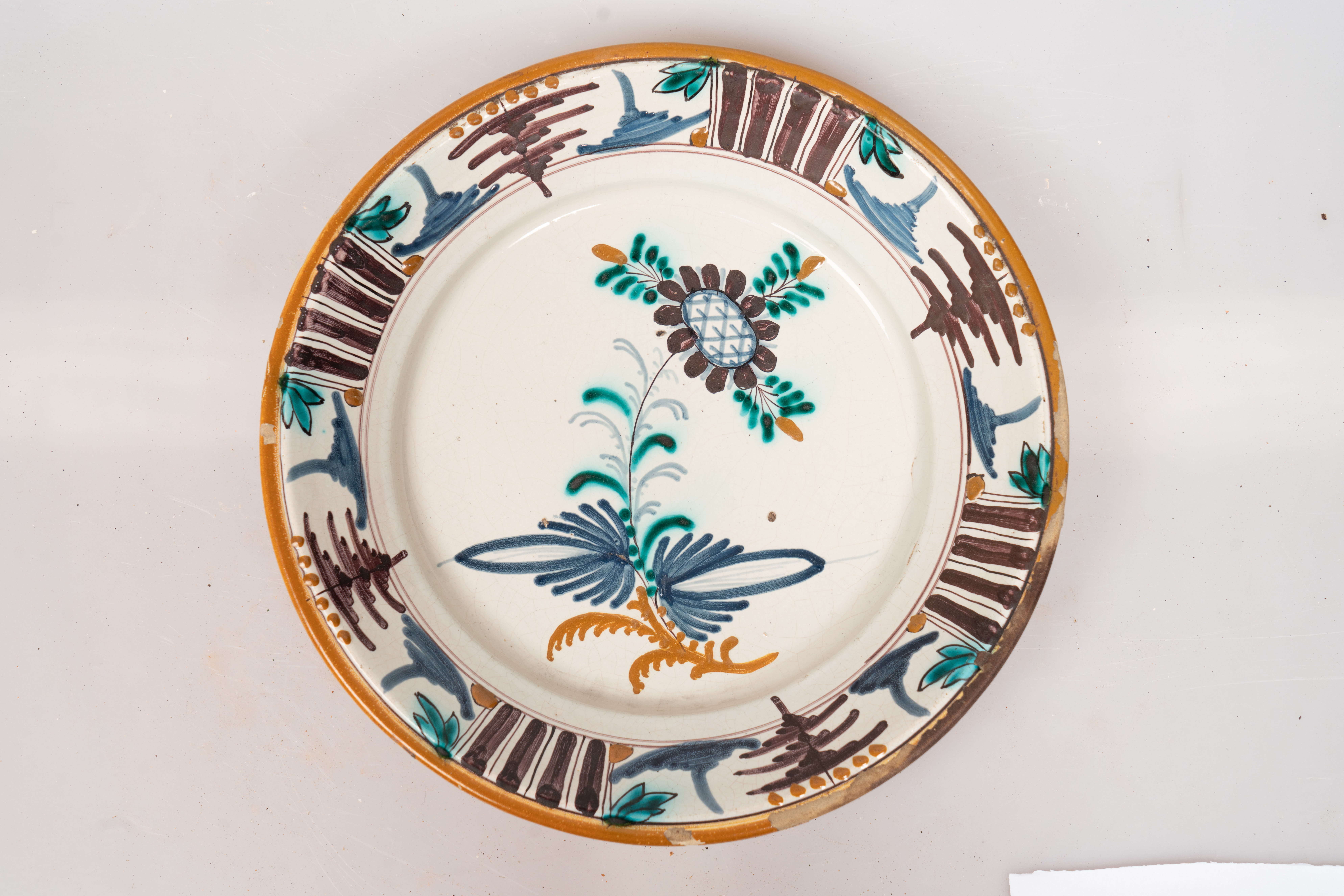 Farfurie de formă aplatizată, cu buza răsfrântă. Decorul, dispus pe un fond alb lăptos, prin pictare, este format dintr-un motiv floral stilizat, dispus central, pe fundul farfuriei, și motive geometrice (puncte galbene, grupuri de dungi paralele de culoare maro-brun, linii subțiri, paralele, linii sub formă de cerc, motivul bradului), dispuse într-un registru continuu pe buza farfuriei. Muchia buzei este marcată cu o dungă de culoare galbenă. Cromatica: alb, verde, brun, albastru, galben-ocru.