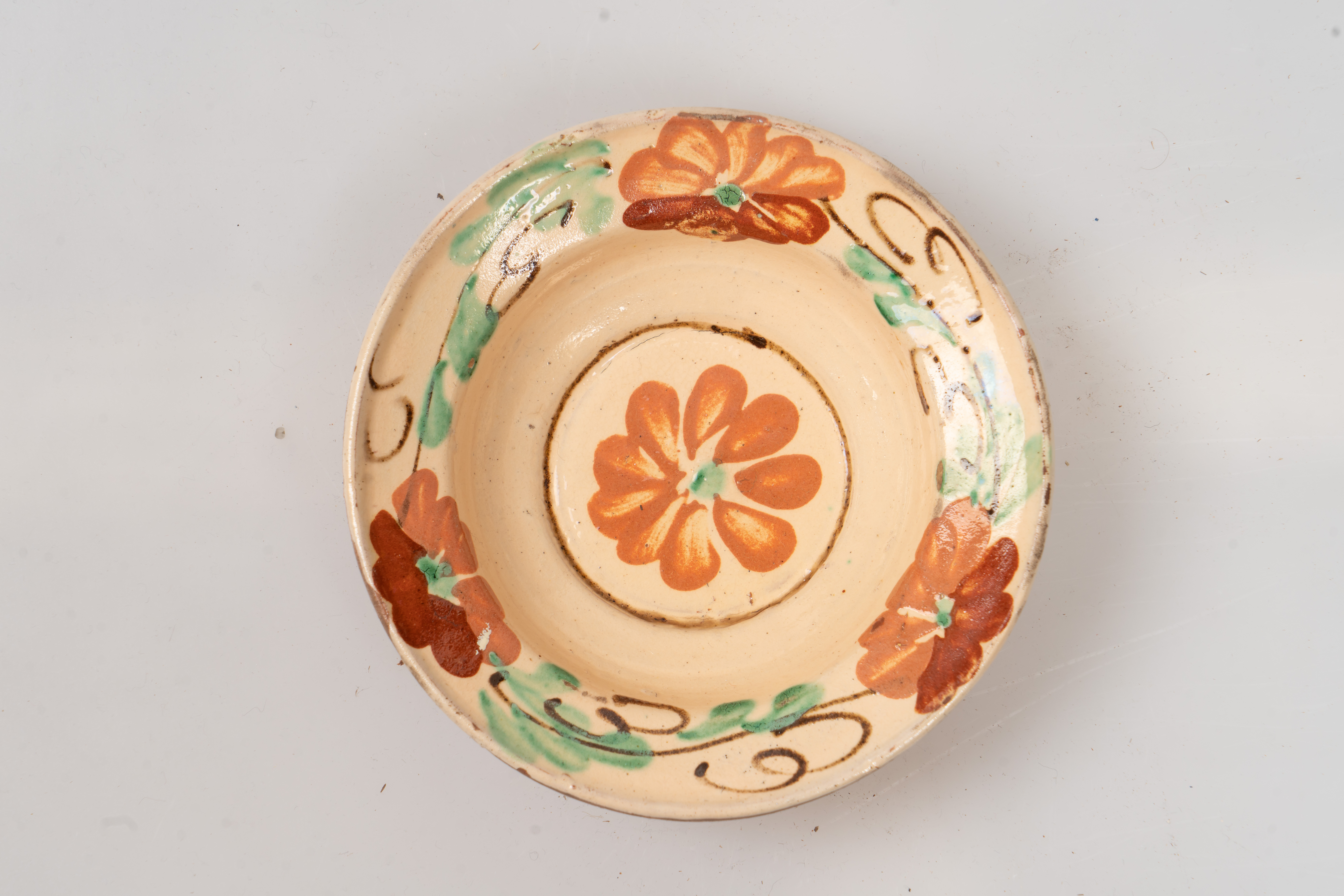 Farfurie adâncă, angobată pe fața interioară cu un strat de humă albă. Este decorată prin pictare cu pensula și cu cornul cu motive florale, fitomorfe și geometrice: trei flori de culoare maro-deschis separate de trei grupuri de frunze verzi cu vrejuri de culoare maro, dispuse pe buza farfuriei și o floare centrală de culoare maro-deschis, înscrisă într-un cerc maro închis - pe fundul farfuriei. Cromatica: alb, verde, maro-deschis, maro-închis. Suprafața ornamentată a farfuriei este acoperită cu un strat de smalț transparent.