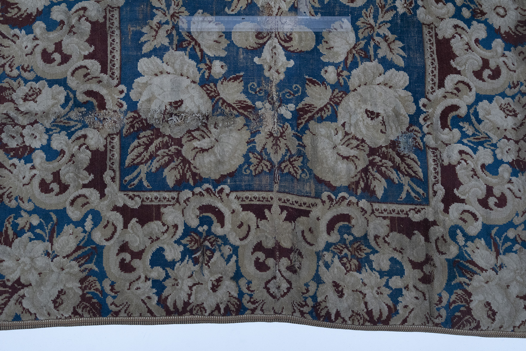Carpet de culoare albastră și roșie. Câmpul central este decorat cu flori alb-crem și frunze roșii, de mari dimensiuni, dispuse în cele patru colțuri, pe fond albastru. În centru se află un medalion stilizat „în oglindă”, cu frunze și vrejuri ondulate. Bordura lată este decorată cu flori și frunze mari de culoare alb-crem, pe fond albastru și roșu.