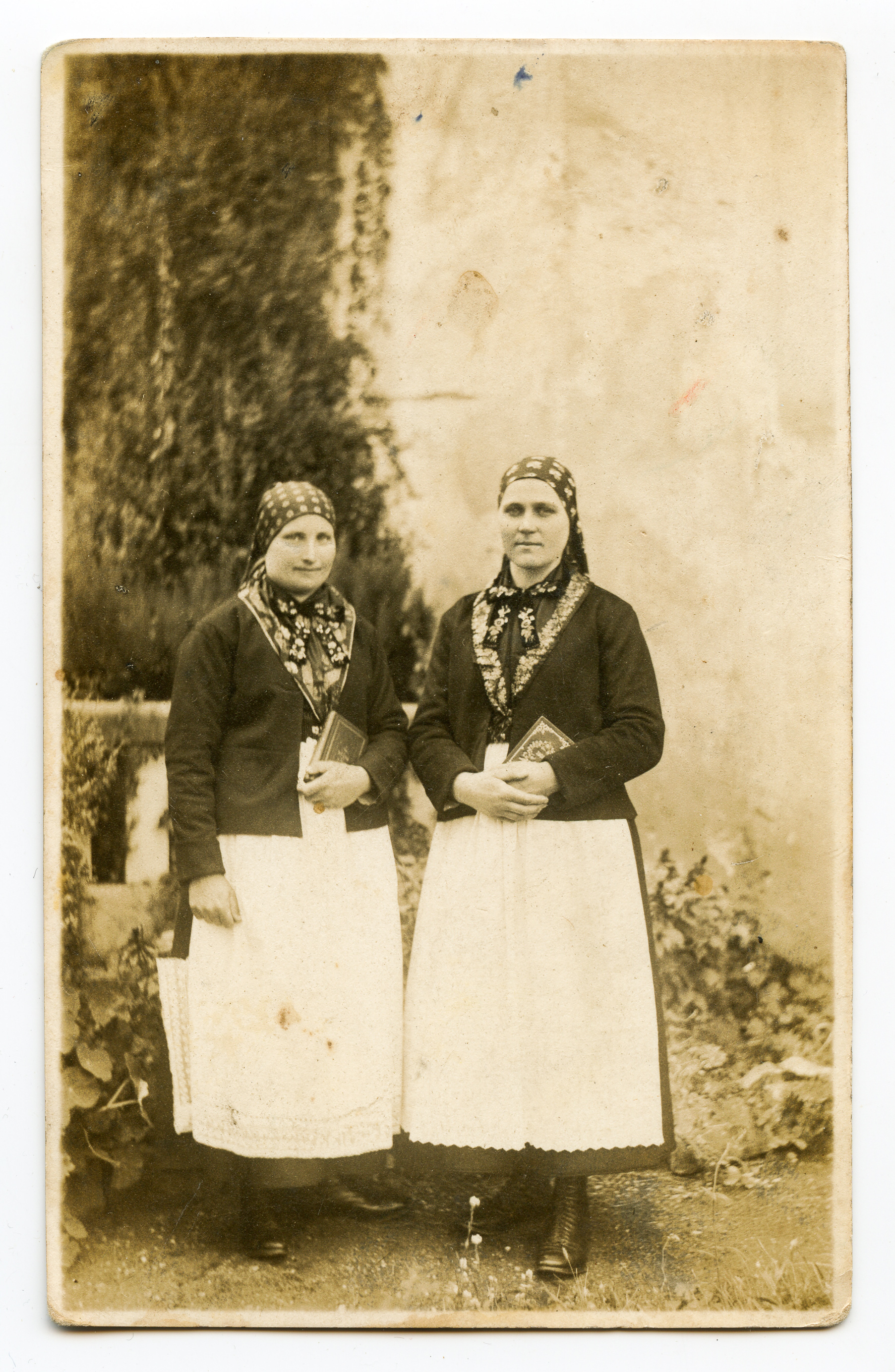 Două femei îmbrăcate în costume de landlerițe. Piesele componente ale costumelor sunt: pe cap baticuri legate la spate înflorate, la gât basmale ornamentate, haine neagre cu gulerul tivit cu material cu motive florale, fuste negre, șorțuri albe cu dantelă, în picioare ghete. Ambele femei țin în mâini câte o carte. Fotografie executată în exteriorul atelierului fotografic. Pe verso rubricatură tip carte poștală; urme de lipire / dezlipire de pe alt suport la mijlocul fotografiei; lipit număr inventar 2837-CL / Turnișor.