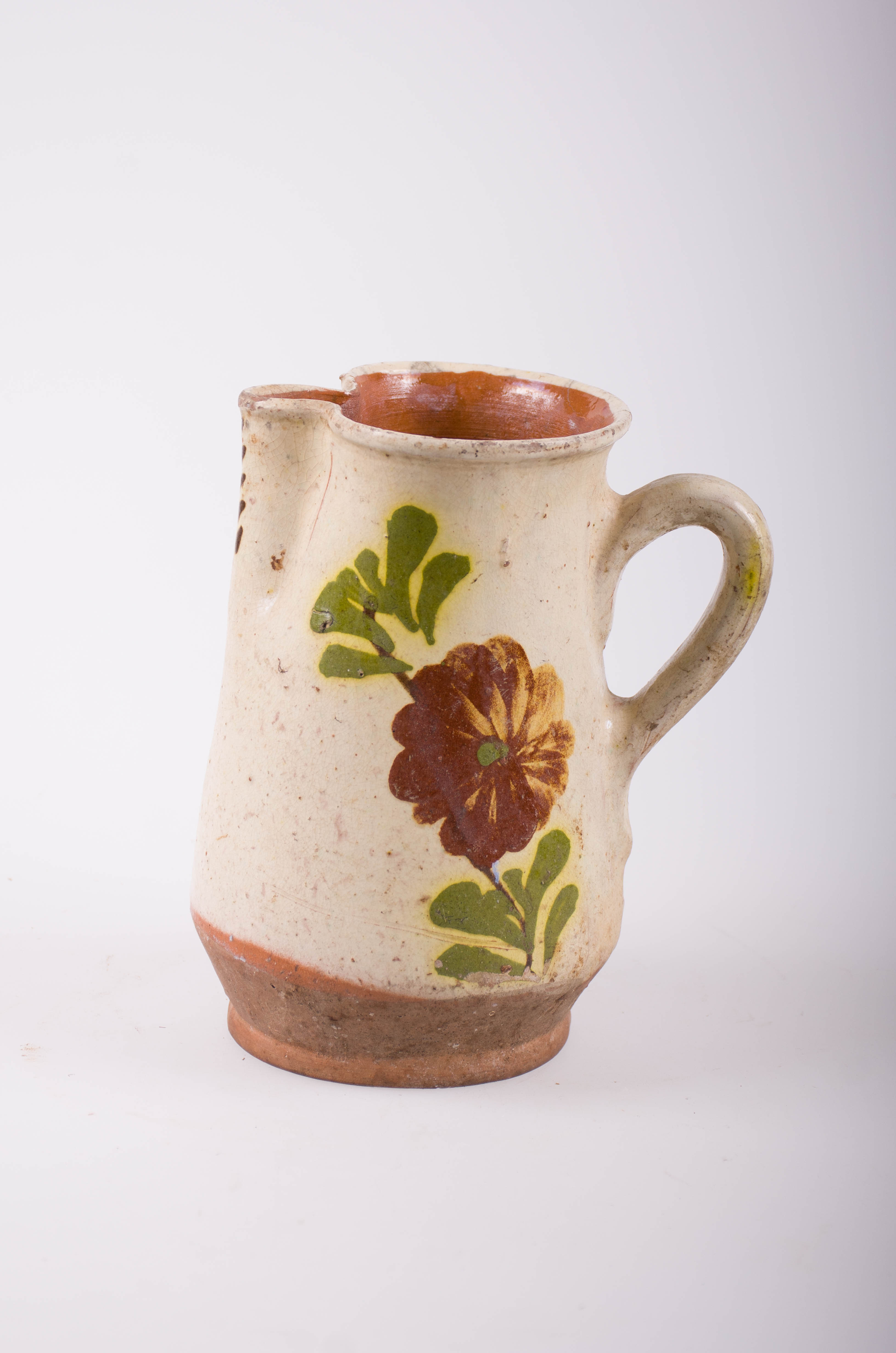 Cană de formă tronconică din ceramică, cu o toartă ce pleacă de sub buza vasului și se termină în partea mediană. Gura modelată cu cioc adâncit; smălțuită în interior și exterior. Decorată cu motive florale și vegetale stilizate. Cromatică: fond: alb-gălbui; motive: verde; albastru; galben.