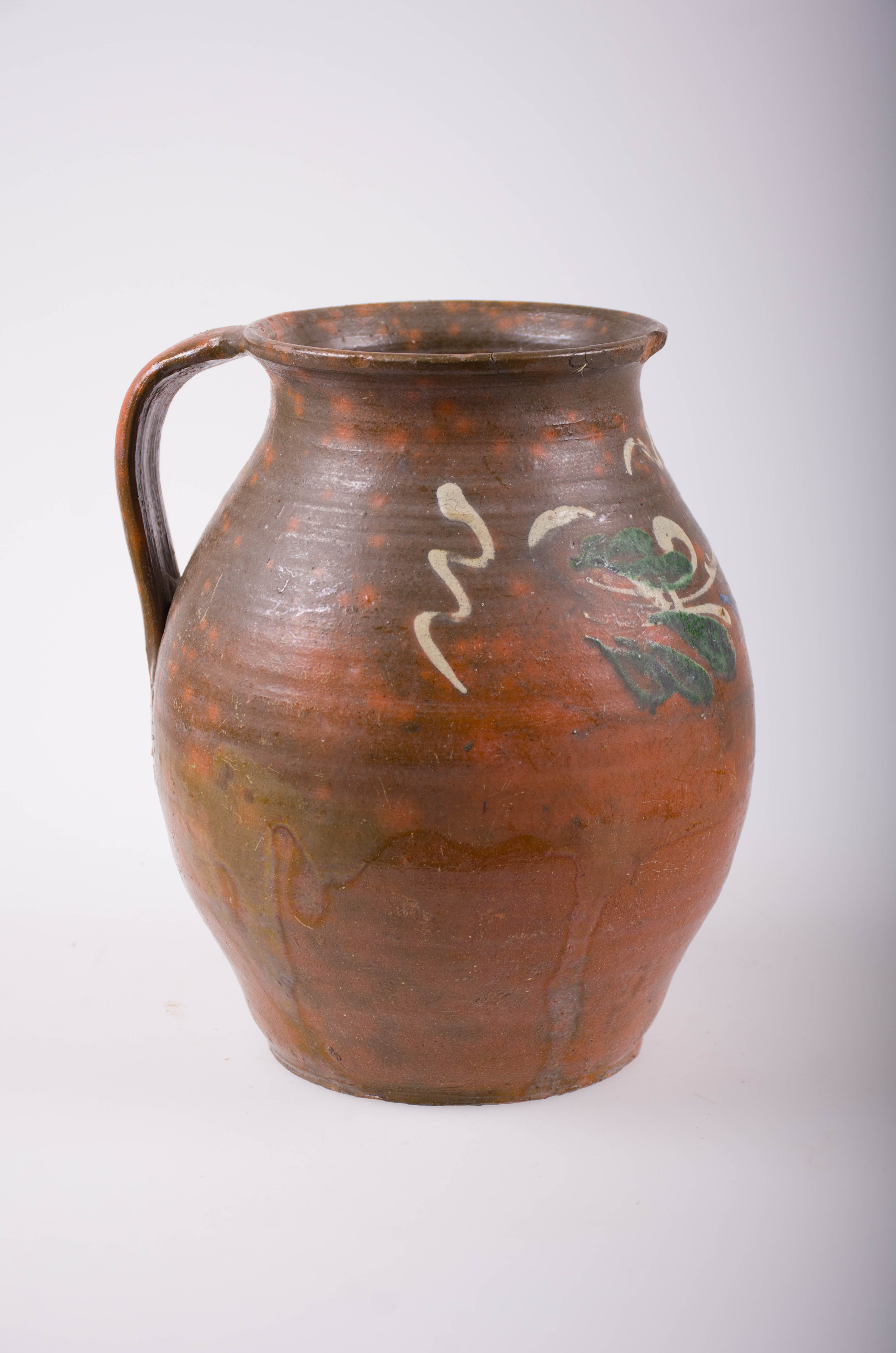 Oală bitronconică cu o toartă, din ceramică. Decorată cu motive florale și geometrice stilizate: linie vălurită. Cromatică: fond maro; motive alb; albastru; verde.