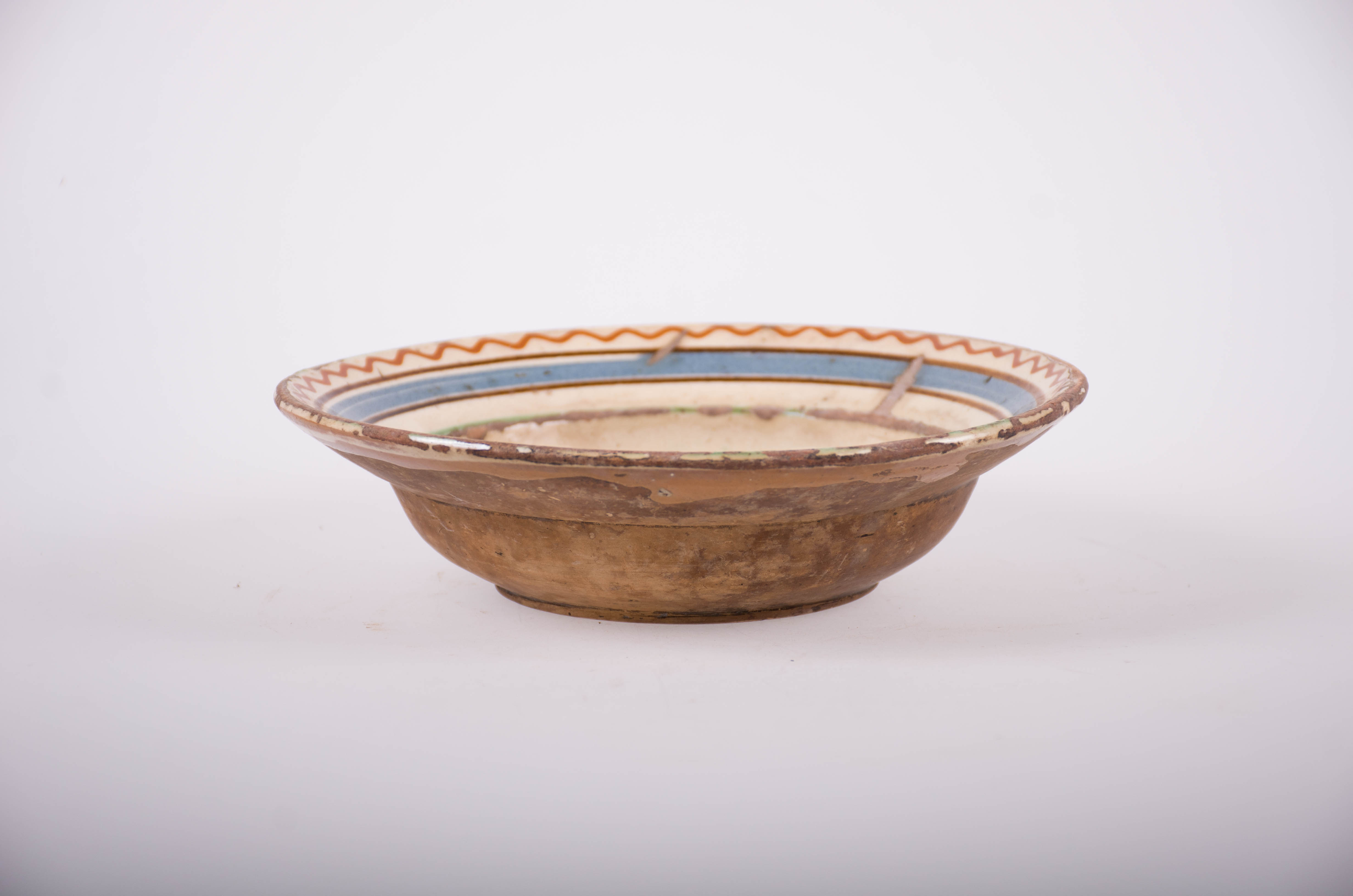 Farfurie din ceramică smălțuită în interior. Decorată cu motive florale și vegetale stilizate, dar și geometrice: linii și linii vălurite pe buza vasului. Cromatică: fond: alb; motive: verde; maro; albastru.