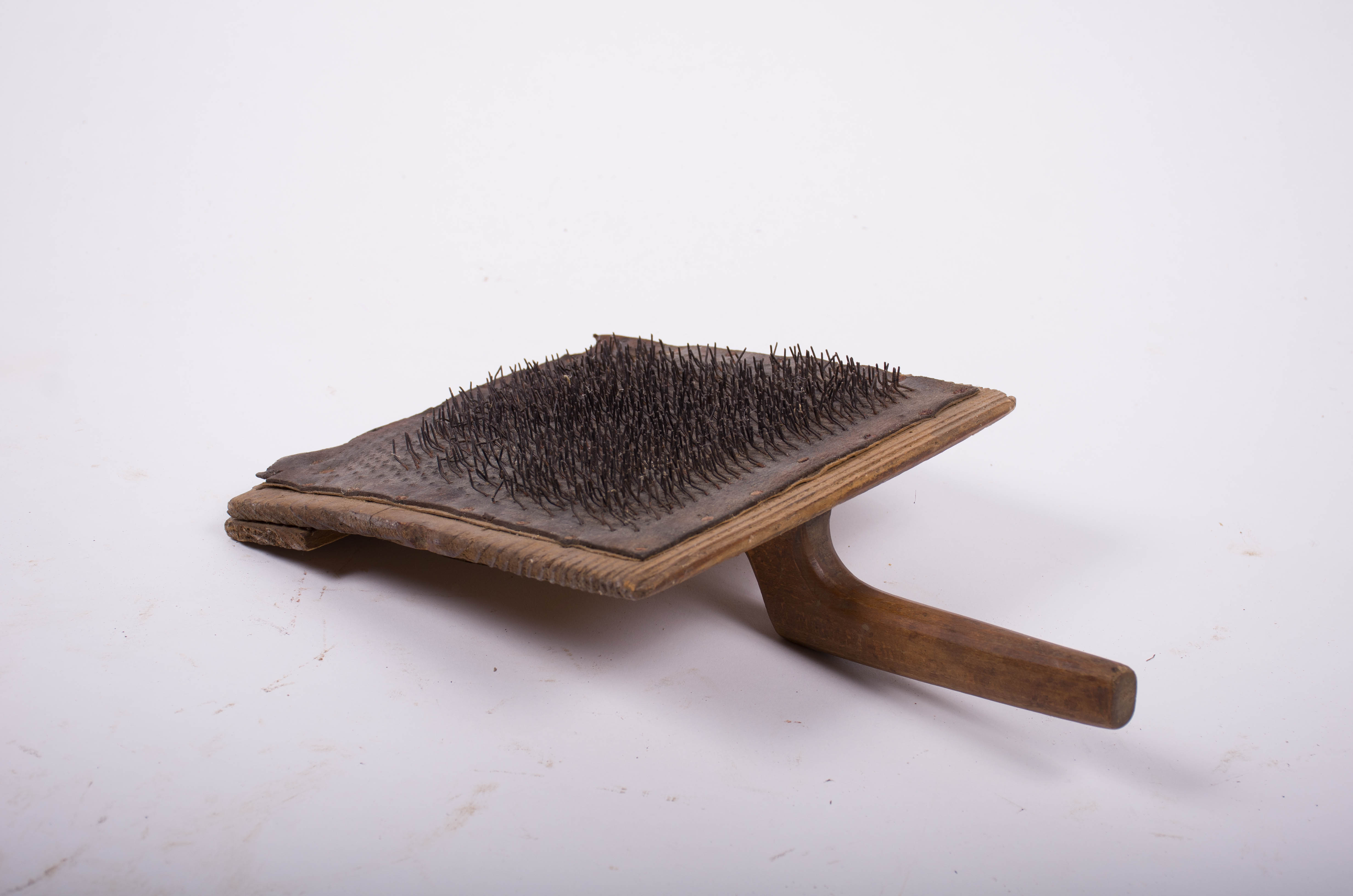 Perie de canepă din lemn și metal de formă dreptunghiulară; pe lemn s-a aplicat o foaie de piele cu dinți de 1/5 cm. Mânerul fixat pe toată lungimea scândurii care ține placa de piele. Placa este fixată prin cuie de metal, o parte din dinții metalici lipsesc. A suferit reparații casnice. Cromatică: culoarea patinată a lemnului.