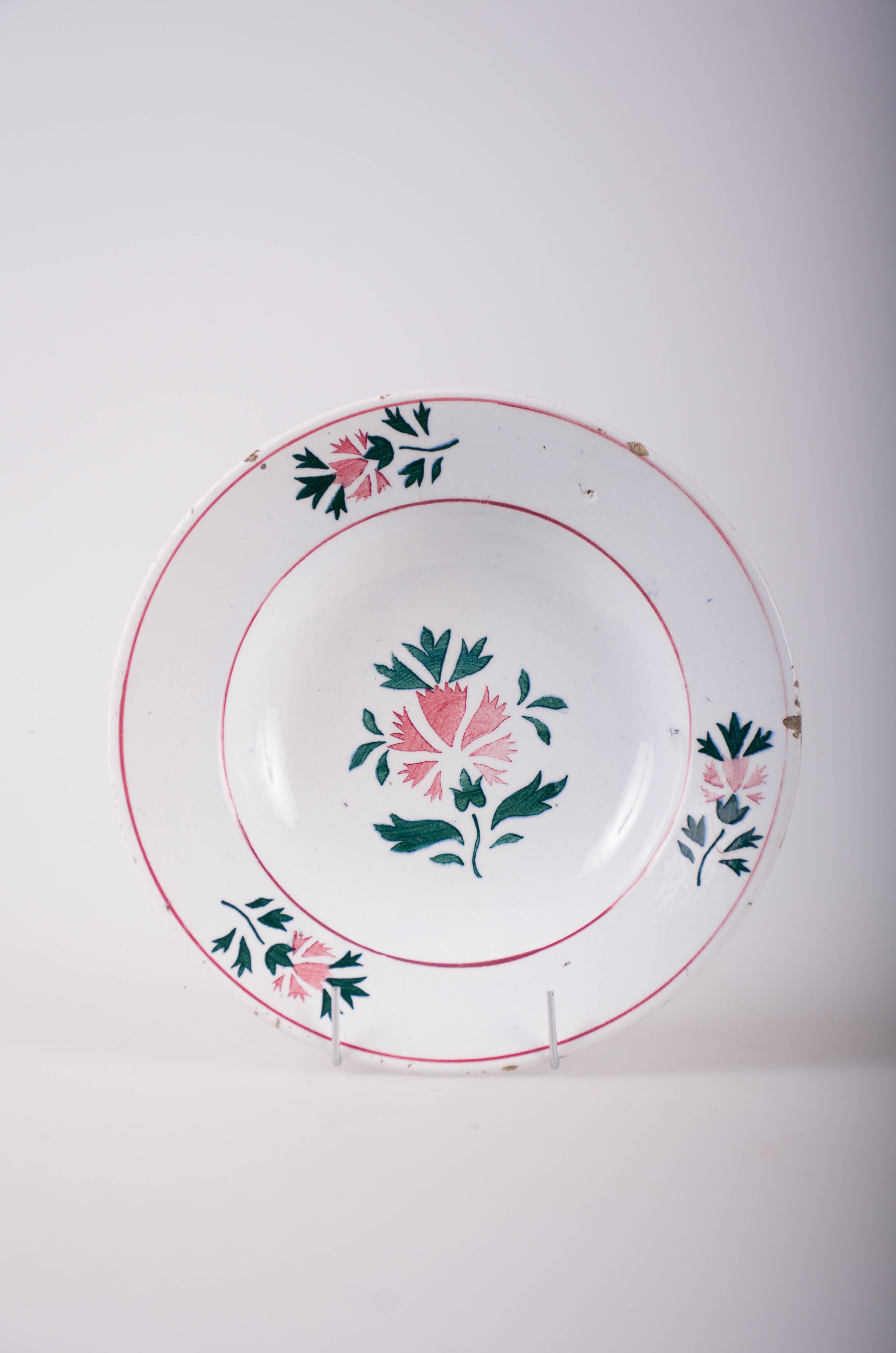 Farfurie de formă tronconică, adâncită; pe fund are găuri pentru agățare. În centru și pe margine este decorată cu motive fitomorfe și florale; pe margine sunt trei flori cu frunze încadrate de două cercuri concentrice; în interior este doar o floare cu frunze. Cromatică: fond: alb; motive: vișiniu; verde.
