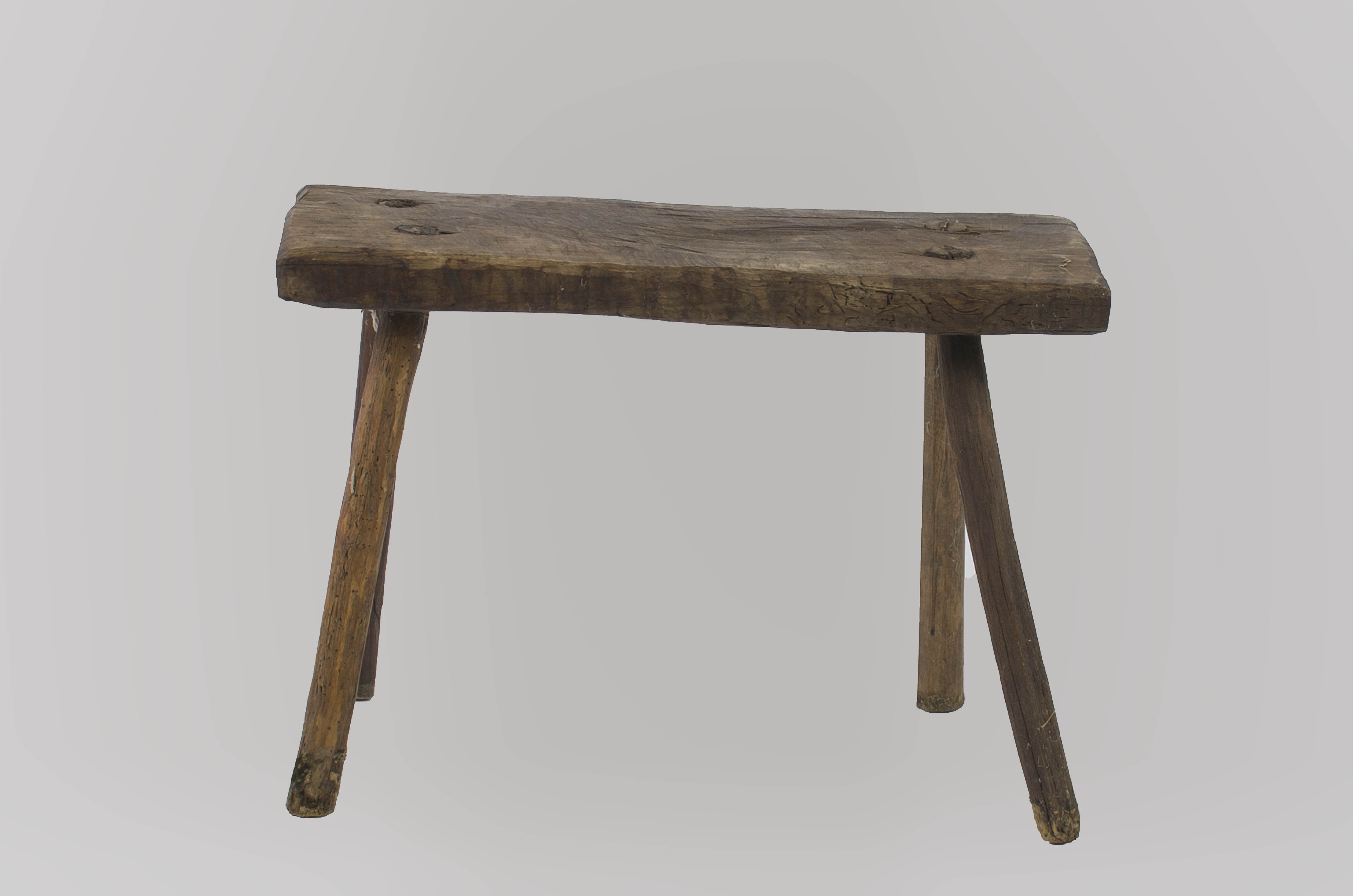 Piesă de mobilier cu șezut dreptunghiular și patru picioare rotunde, puternic evazate. Picioarele sunt fixate în patru găuri realizate în corpul șezutului. Cromatică: culoarea patinată a lemnului.