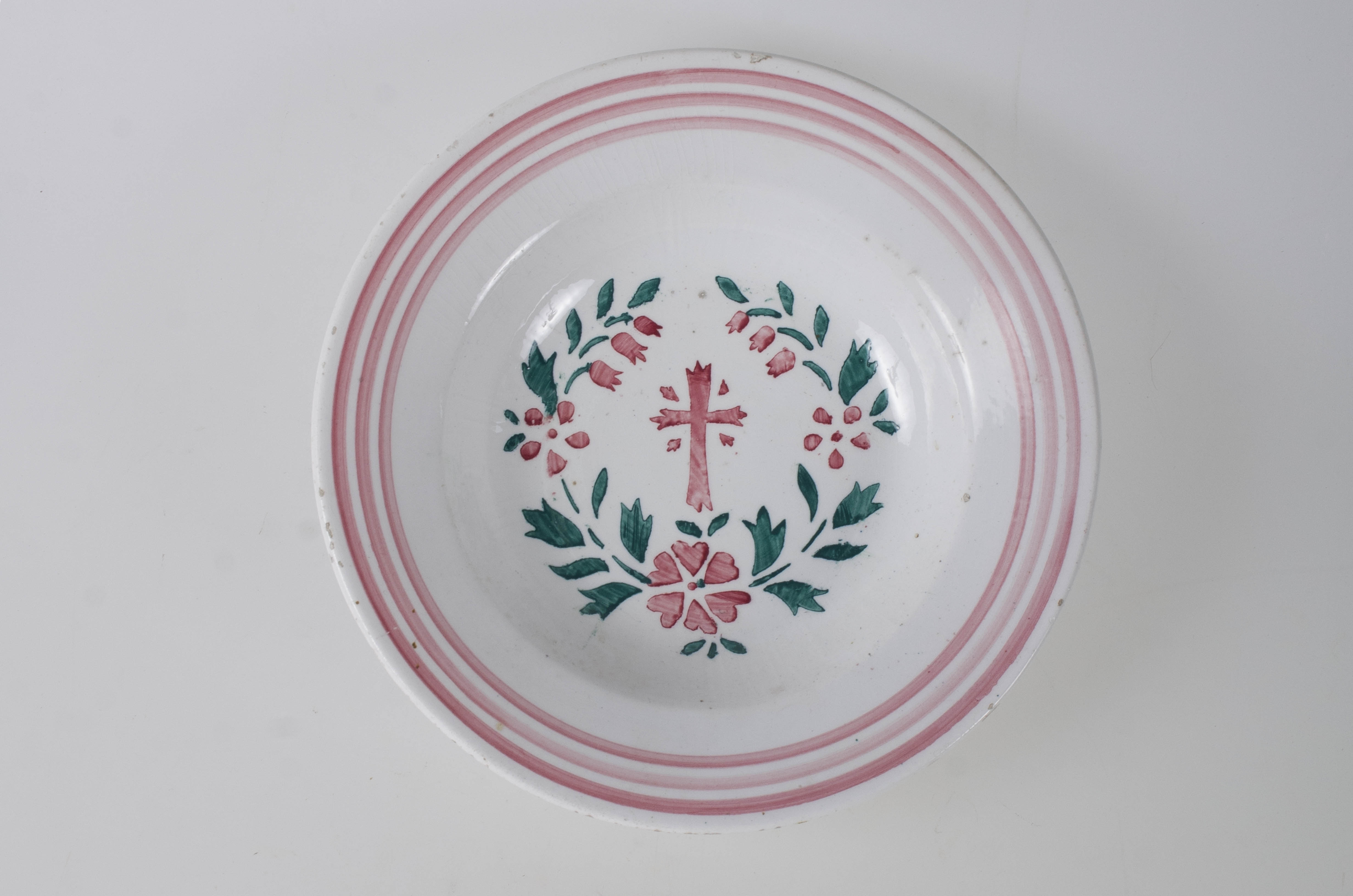 Farfurie de formă tronconică, adâncită; pe margine este decorată cu motive geometrice: trei cercuri concentrice. În centru este pictată o cruce, încadrată de flori și frunze dispuse circular. Pe exteriorul vasului de la bază spre buză se disting trei profile circulare. Cromatică: fond alb; motive: roșu; verde.