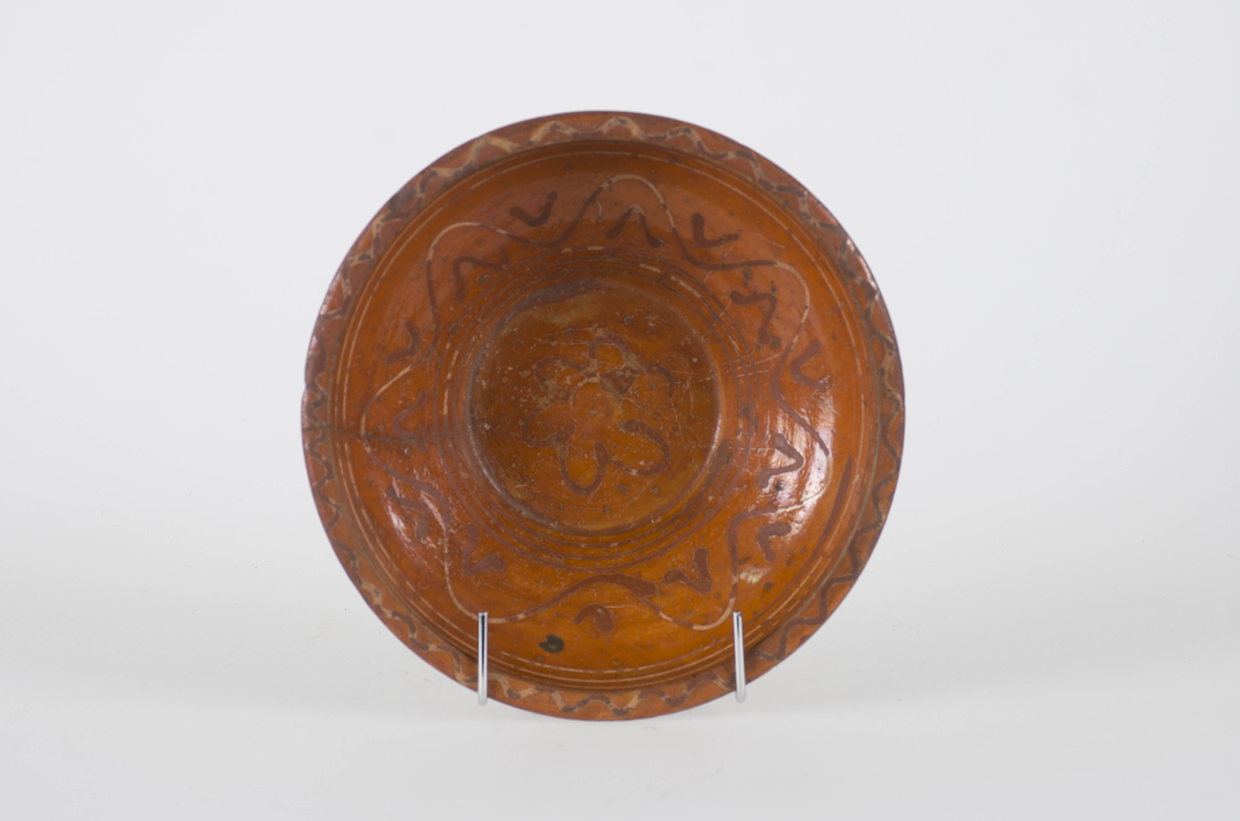 Blid ceramic, tronoconic, smălțuit, de dimensiuni medii, cu marginile puțin evazate și buza dreaptă. Decorul geometric și vegetal stilizat este compus din: o floare cu șase petale, aflat în fundul vasului și patru linii concentrice în marginea inferioară, care sunt înconjurate de o dungă în valuri și de paisprezece linii scurte, tot în valuri formând astfel o floare sau un simbol solar. Marginea superioară a vasului a fost ornamentată cu trei linii concentrice, iar buza cu o linie în valuri. Cromatică: fondul este cărămiziu iar decorul este maro închis și alb-crem. Smălțuirea vasului a fost realizată doar la interior.