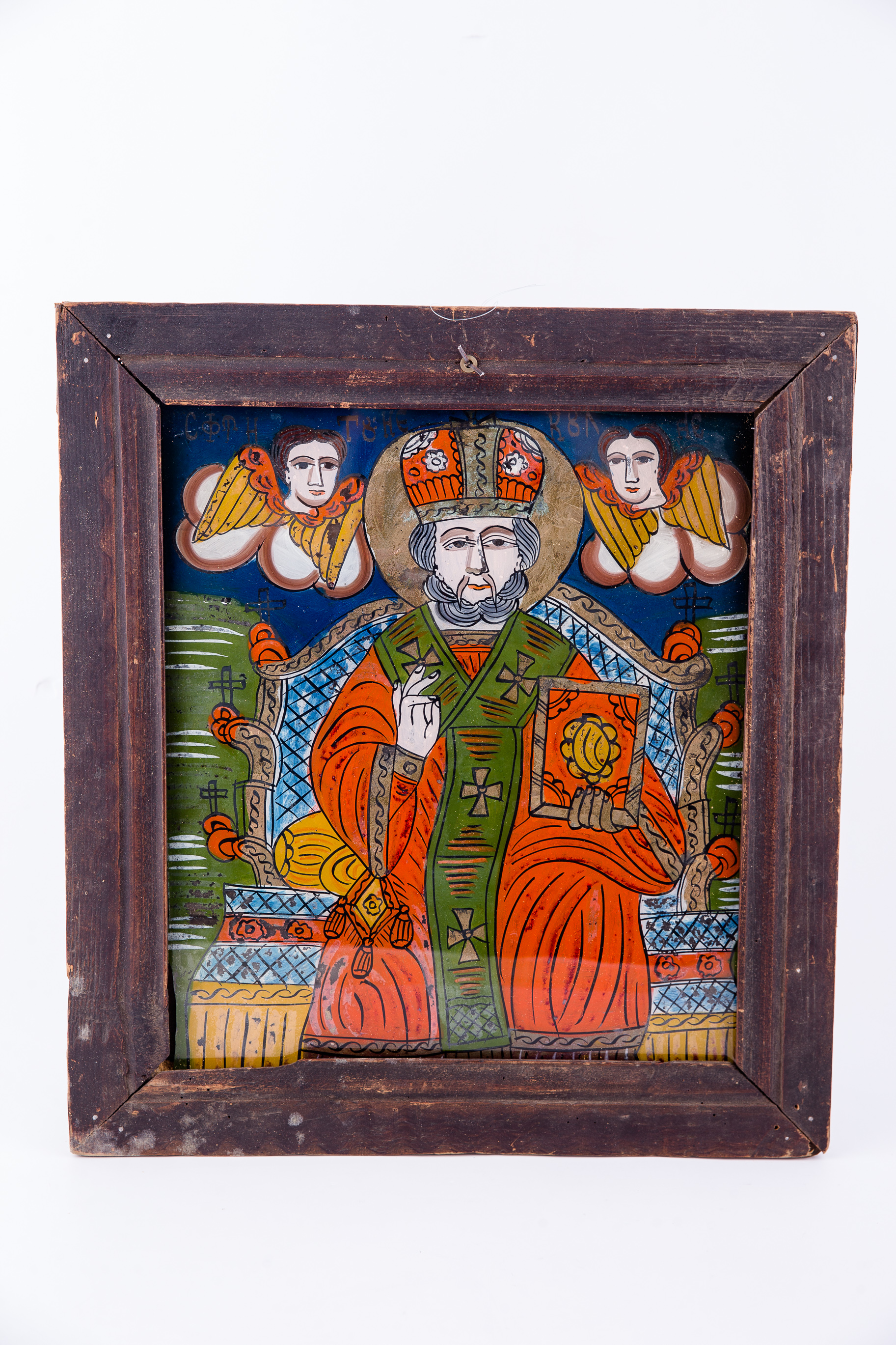 Sfântul Mare Ierarh Nicolae, făcător de minuni, îmbrăcat în veșminte liturgice, de ierarh, sacos și felon rosu vermillon-coral, cu epitrahil-patrafir verde (spanac, avocado) cu patru cruci. Ține în mâna stângă Sfânta Evanghelie și cu dreapta Binecuvintează. Este unul dintre cei mai populari și iubiți sfinți, ocrotitor al caselor, familiilor și copiilor. Are barbă lungă, albă și mithră arhierească și aureolă. Este așezat pe un tron bogat ornamentat, de arhiereu. Tronul este asemenea unui palat, cu o arhitectură de biserică, cu cruci și turnuri. În registrul superior, îndepărtat, sunt reprezentate pe nouri albi două chipuri de îngeri serafimi, cu aripi galbene. Fondul este albastru senin, în registrul superior. Desenul este fin conturat. Cromatica: rosu vermillon-coral, verde (spanac, avocado), alb, albastru. Icoana este de Țara Oltului. Inscripiția în chirilică este Sfântul Nicolae.
