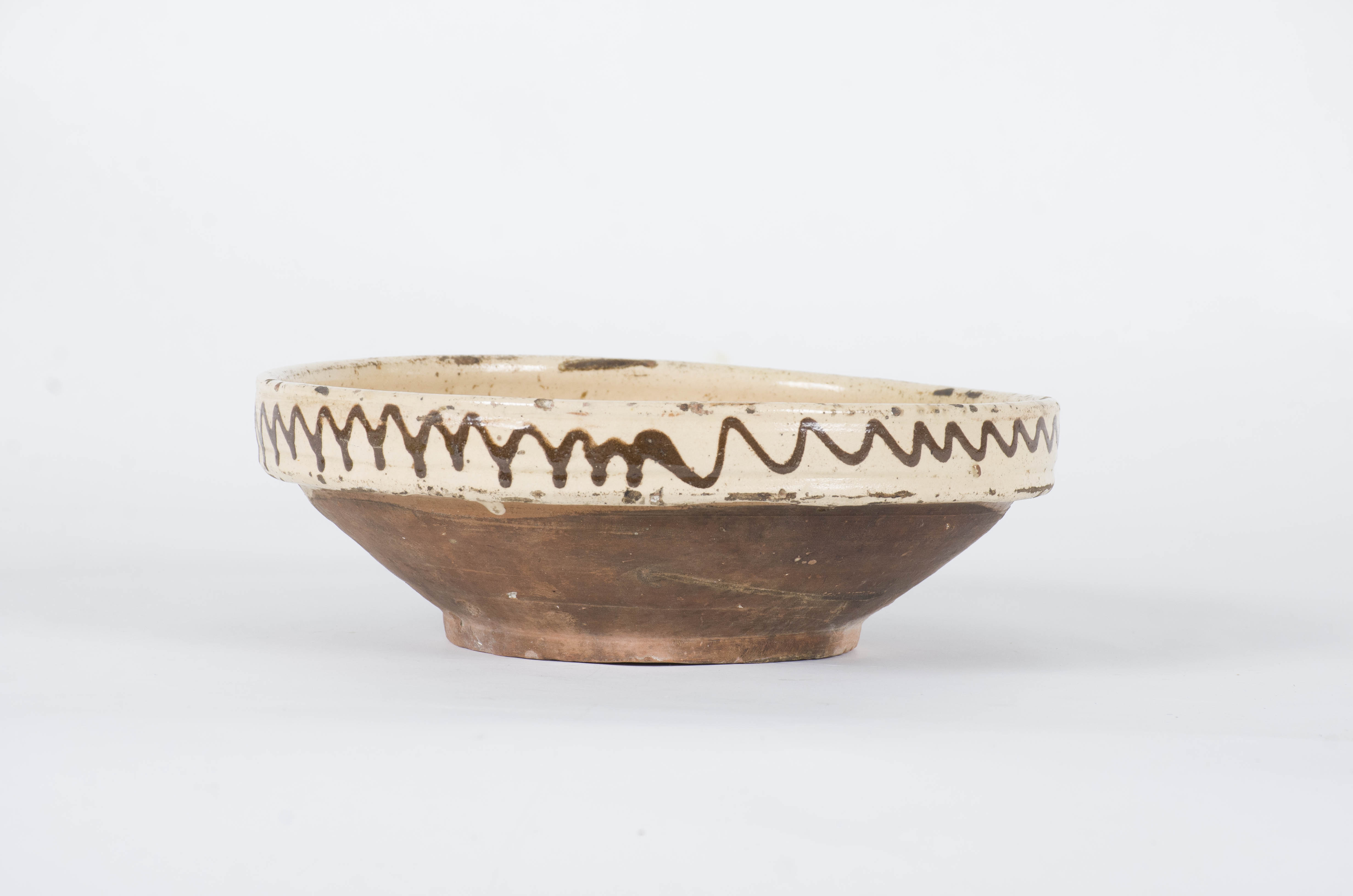 Ceramică de formă tronconică, foarte adâncită, cu buza înaltă și ieșită în afară față de corp; este smălțuit în interior și exterior (doar buza); în interior, în centru este decorat cu o floare înscrisă într-un cerc, iar pe pereții interiori cu două flori despărțite de două registre formate din mai multe linii ondulate, încadrate de o linie; pe marginea exterioară este decorat cu o linie ondulată. Cromatică: fond interior crem; fond exterior maro; motive: maro; roșu; verde; cărămiziu închis.