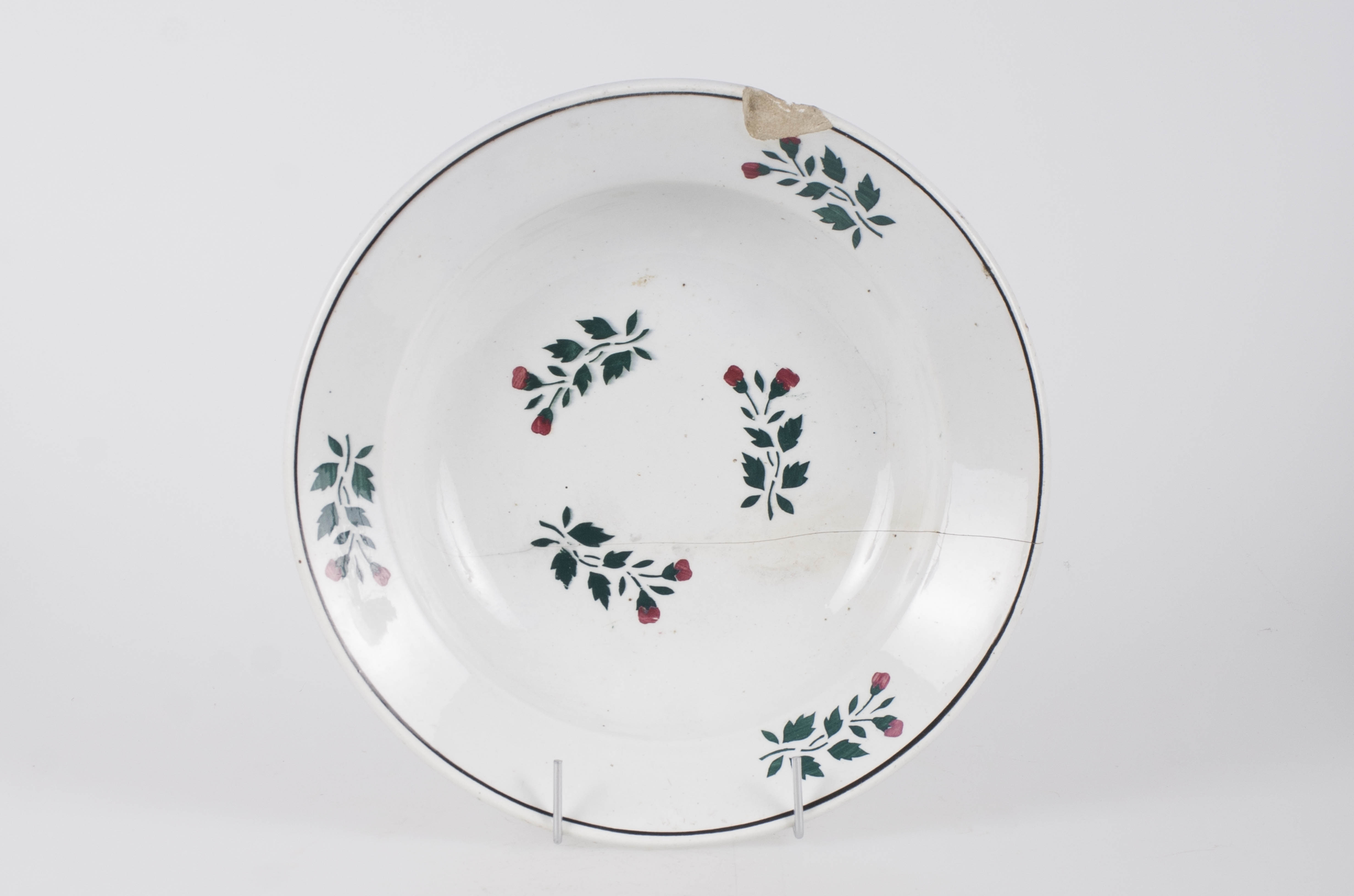 Farfurie din faianță smălțuită cu smalț alb. Vasul este de formă circulară, ușor adâncită. Pe fundul vasului decorul este floral-vegetal. Pe buza vasului se identifică trei flori, un decor geometric (cerc) ce încadrează decorul floral. Pe fundul vasului se identifică marca ”WILHELMSBURG”. Cromatică: fond alb; motive: verde; roșu.