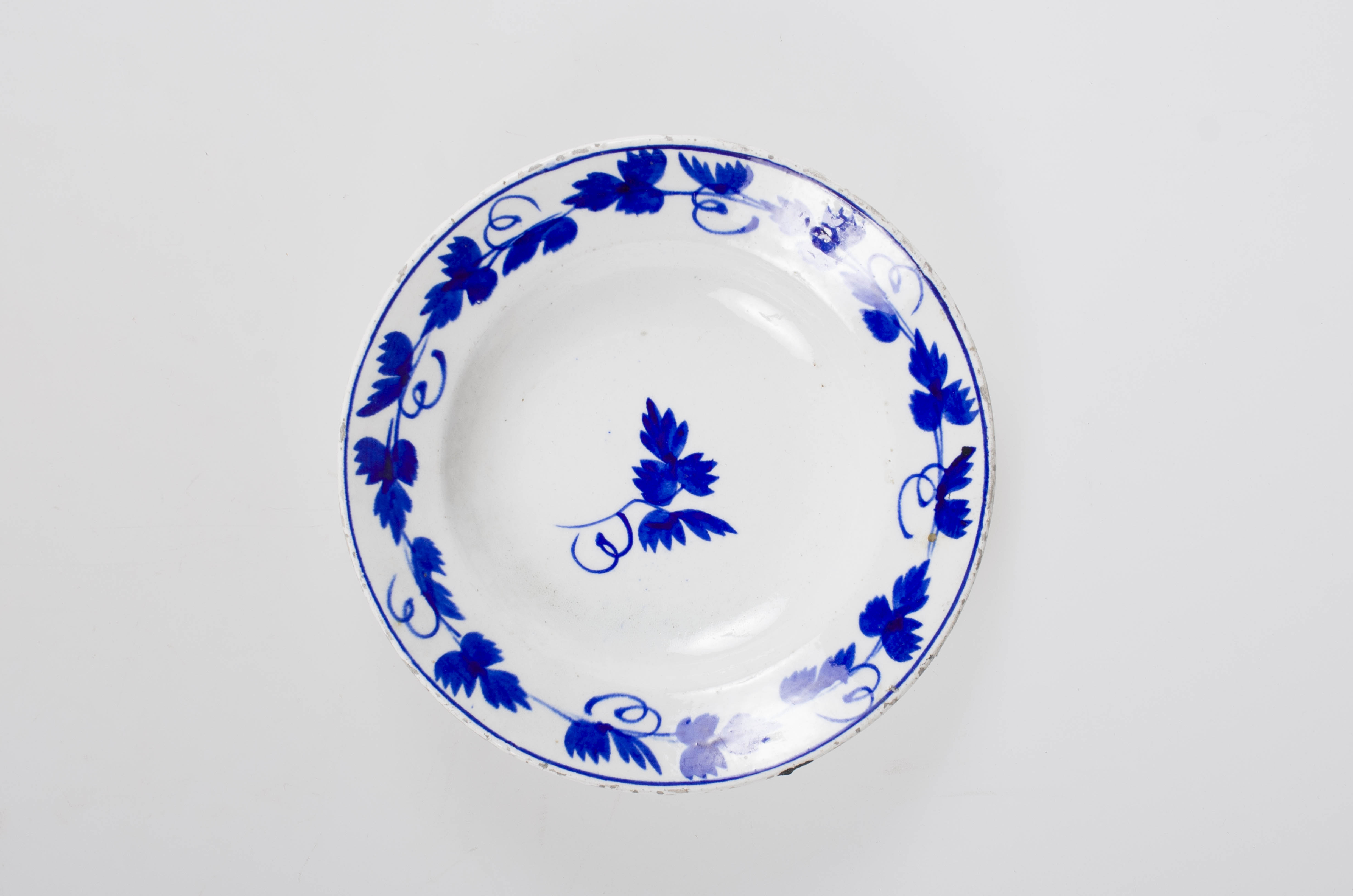 Obiect de uz casnic de formă tronconică. Pe fond alb se regăsește un ornament albastru: central două frunze de viță de vie. Pe margine farfuria este decorată cu frunze de viță de vie cu vrej și cu un cerc albastru. Cromatică: fond: alb; motive: albastru.