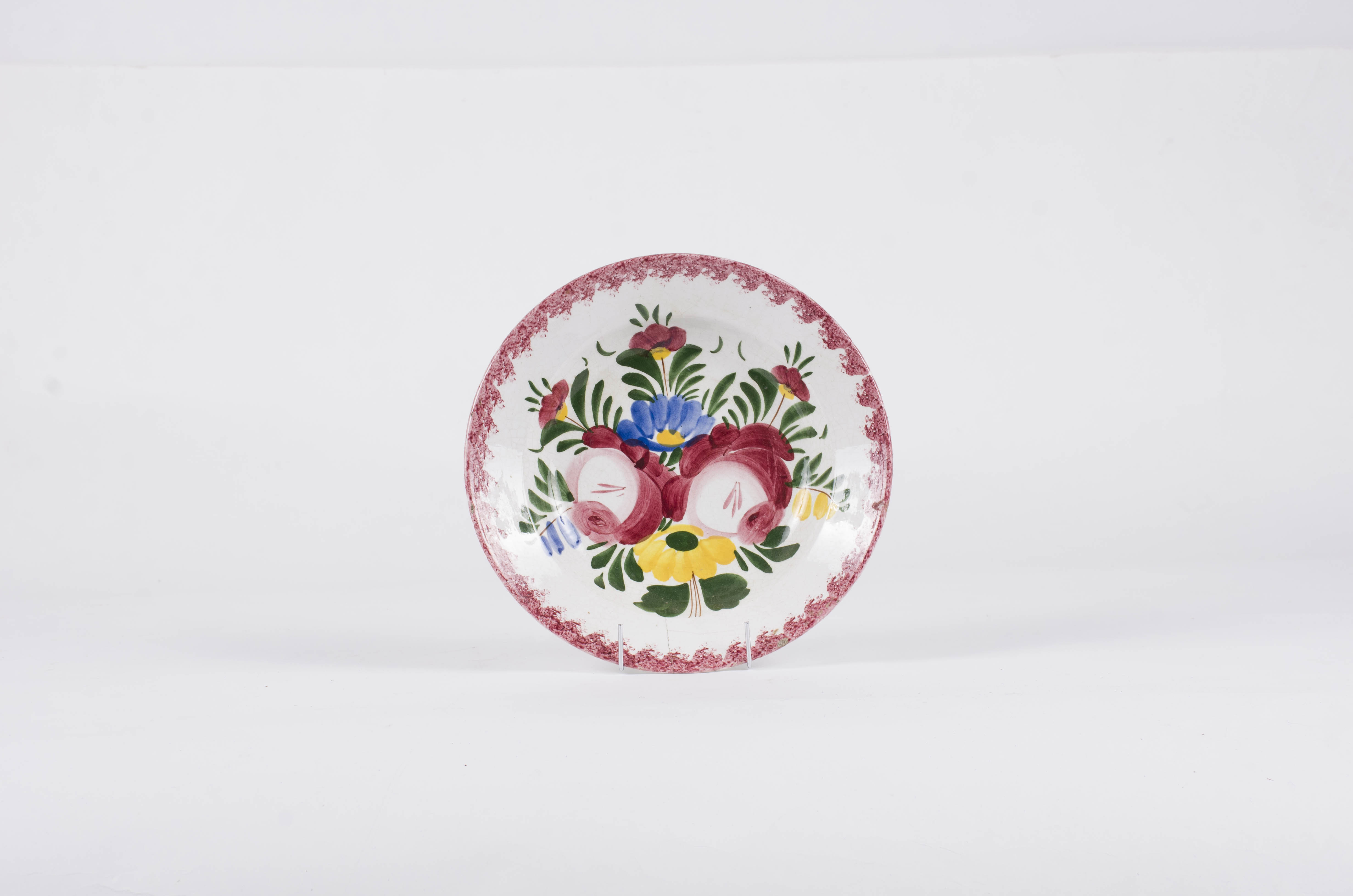 Vasul este de formă tronconică fiind smălțuit interior-exterior. Este confecționat din faianță Decorul este format din motive florale pictate pe fond alb; gura este decorată în stropi de culoare vișinie iar baza farfuriei este decorată cu motive florale. Se identifică șapte flori alcătuind motivul decorativ pe baza farfuriei. Pe spate inscripția este indescifrabilă. Cromatică: galben; albastru; verde; vișiniu; alb;