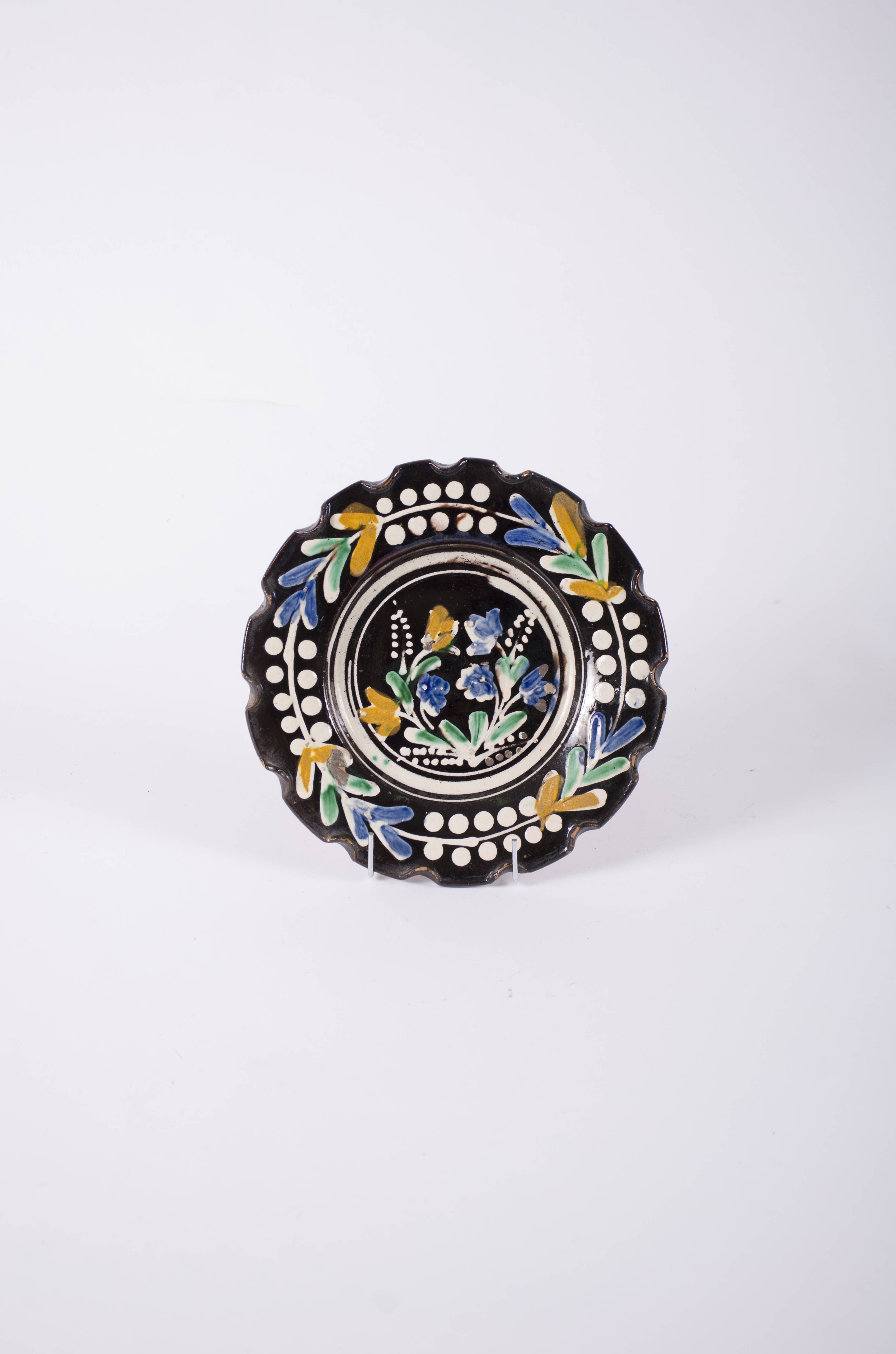 Vasul de ceramică este de forma unui disc plat cu margini ondulate prin apăsare cu degetul. Farfuria este smălțuită în interior. Este decorată în interior cu trei cercuri concentrice în interiorul cărora se găsesc motive florale; pe margine este decorat cu patru flori despărțite de patru crenguțe cu boabe (o linie încadrată de două șiruri de puncte). Cromatică: fond maro; motive: alb; portocaliu; verde; albastru.
