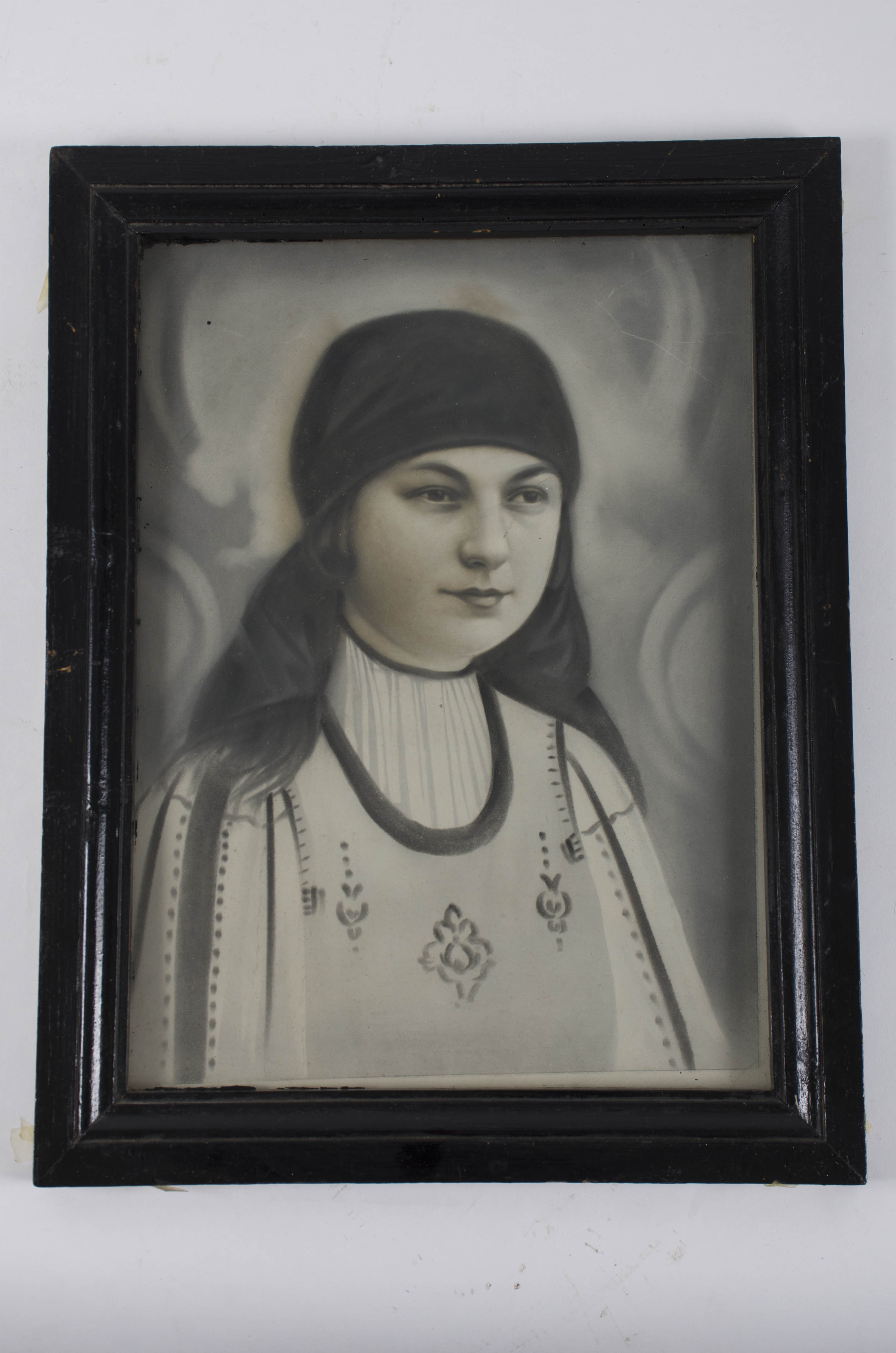 Desen în cărbune după o fotografie, reprezentând pe învățătoarea Maria Poplăcean, soția înv. Nicolaie Poplăcean, îmbrăcată în costum popular cu o năframă pe cap. Având în vedere vârsta din imagine (20 - 30 ani) deducem că fotografia a fost realizată între 1928 - 1938 (Învățătoarea Poplăcean Maria a trăit între 1908 - 1973). Desenul este protejat în față de o sticlă fiind prins de ramă cu ajutorul unor cuie. În spate este protejată de o bucată de carton, lipită direct de ramă, acoperind-o în spate în totalitate. De acest carton pe ramă în partea superioară în spate este prinsă o mică bucată metalică care are la capătul superior un inel de formă triunghiulară, folosit pentru agățătoarea desenului. Rama este vopsită în culoarea maro închis. În față, rama prezintă două registre; unul drept neted și altul care se retrage spre fotografie.