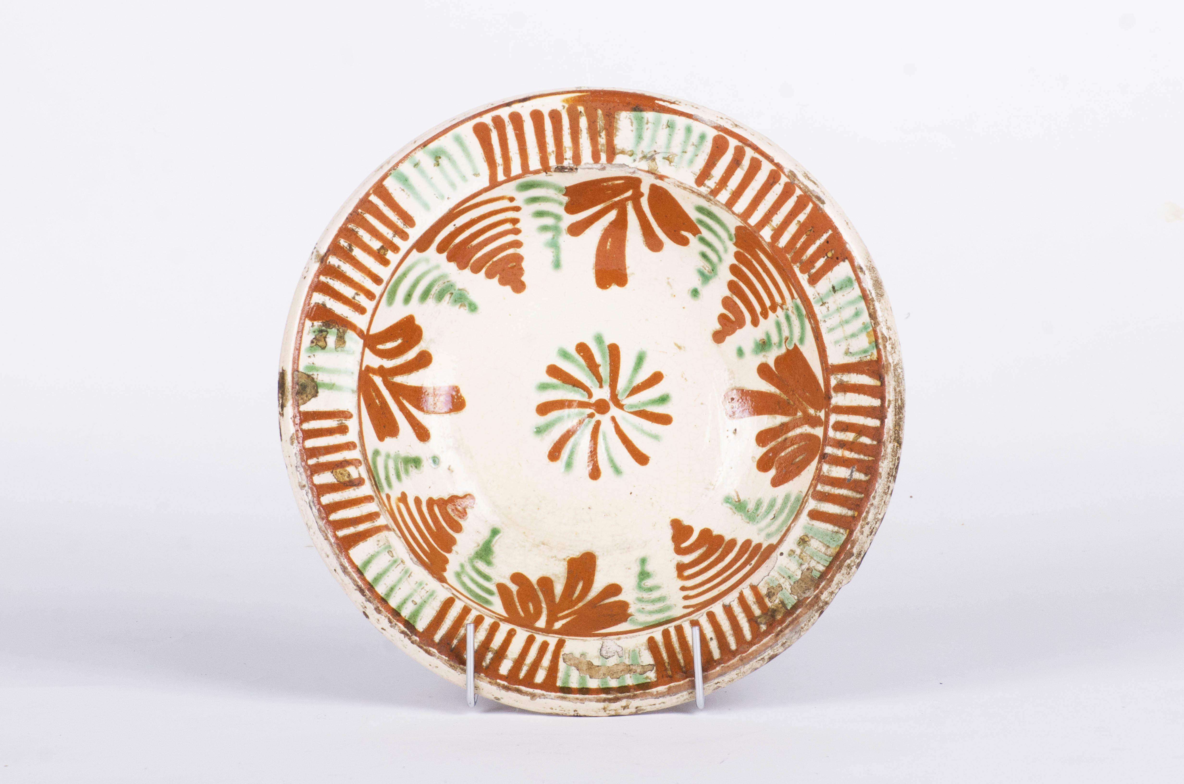Blidul ceramic este rotund, adânc, cu pereții evazați și cu buza răsfrântă înafară. Fața este smălțuită și ornamentată. Centrul blidului este marcat de o rozetă spre care converg ornamentele florale stilizate. Între cele două benzi ce marchează buza blidului sunt benzi de hașuri succesive în maro și verde. Cromatică: fond: alb-crem; motive: maro; verde.