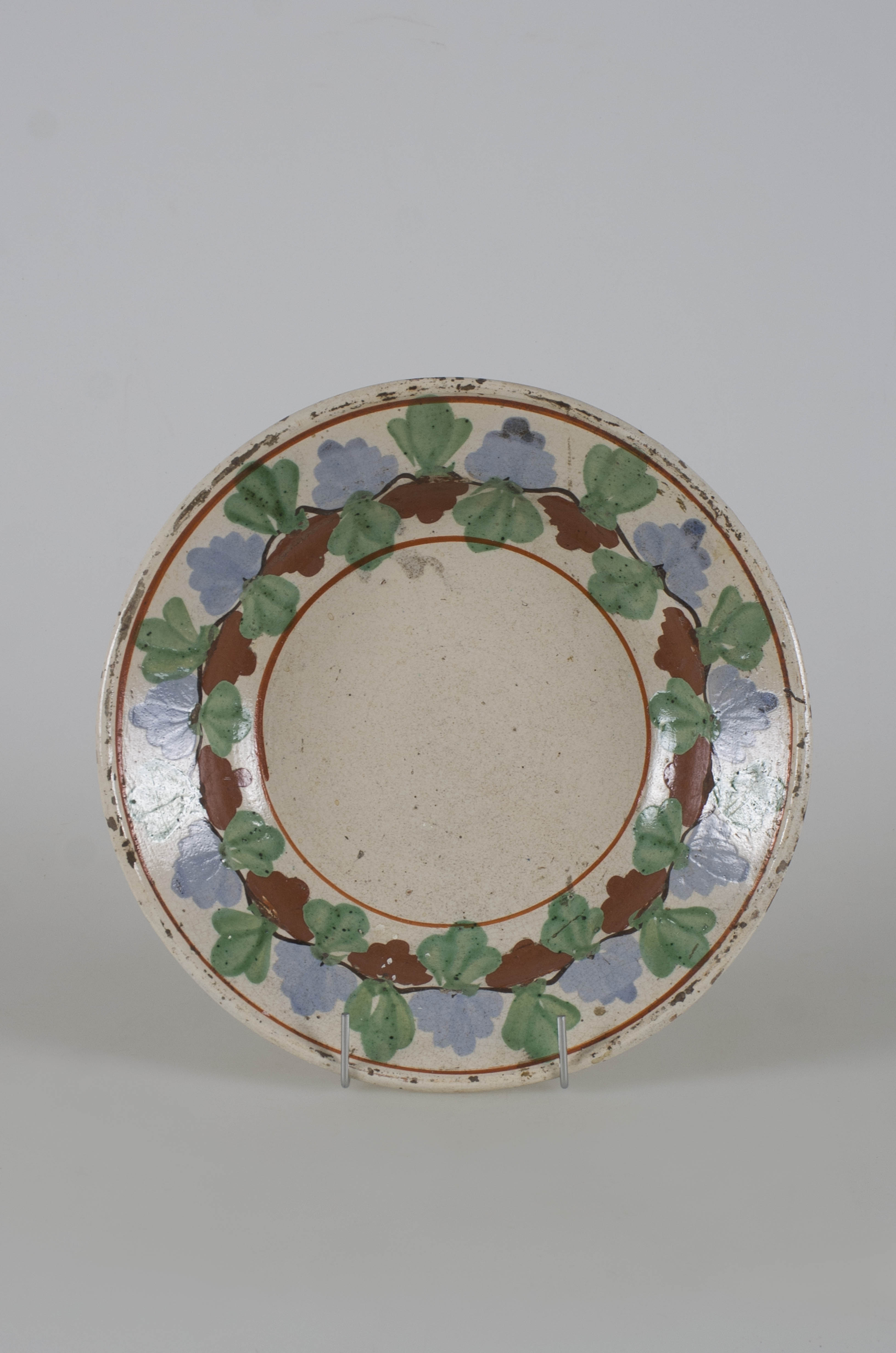 Vasul ceramic are formă circulară; adâncit și prezintă marginile evazate. Este smălțuit pe interior și pe buza vasului. În interior, pe marginea farfuriei, este ornamentat cu motive florale stilizate dispuse într-un registru încadrate de două linii concentrice maro. Cromatică: fond: alb; motive: verde; albastru deschis; maro.