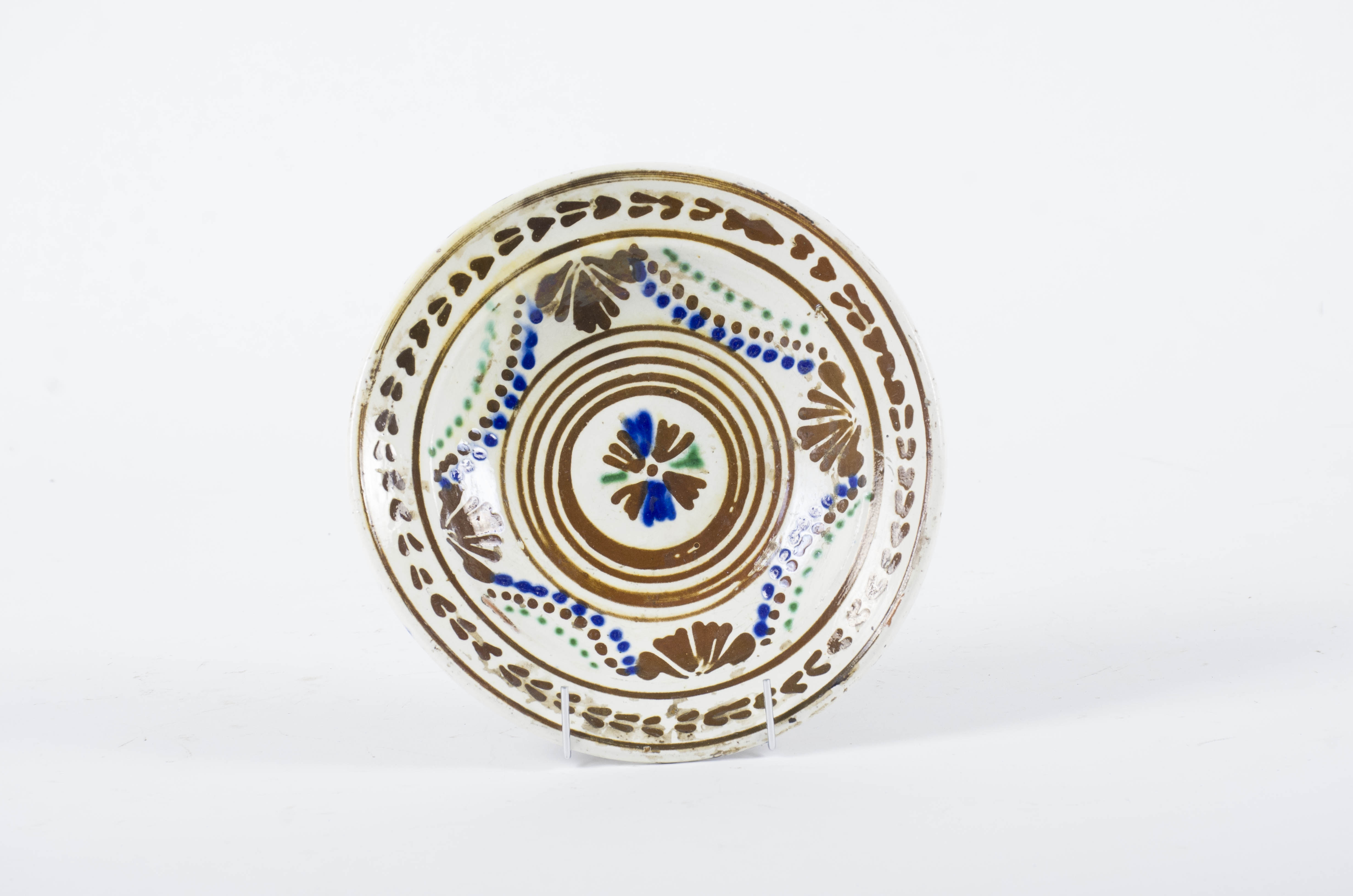Blidul ceramic este rotund, adânc, cu pereții evazați și cu buza răsfrântă înafară. Fața este smălțuită și ornamentată. Buza este marcată de două cercuri concentrice în interiorul cărora se găsesc motive florale stilizate monocrome. În centrul blidului găsim o floare stilizată circumscrisă într-o succesiune de cinci cercuri concentrice. Acestea din urmă, la rândul lor, sunt încadrate de o succesiune formată din motive florale stilizate și punctiforme ce descriu împreună un romb. Cromatică: fond: alb-crem; motive: maro; albastru; verde.