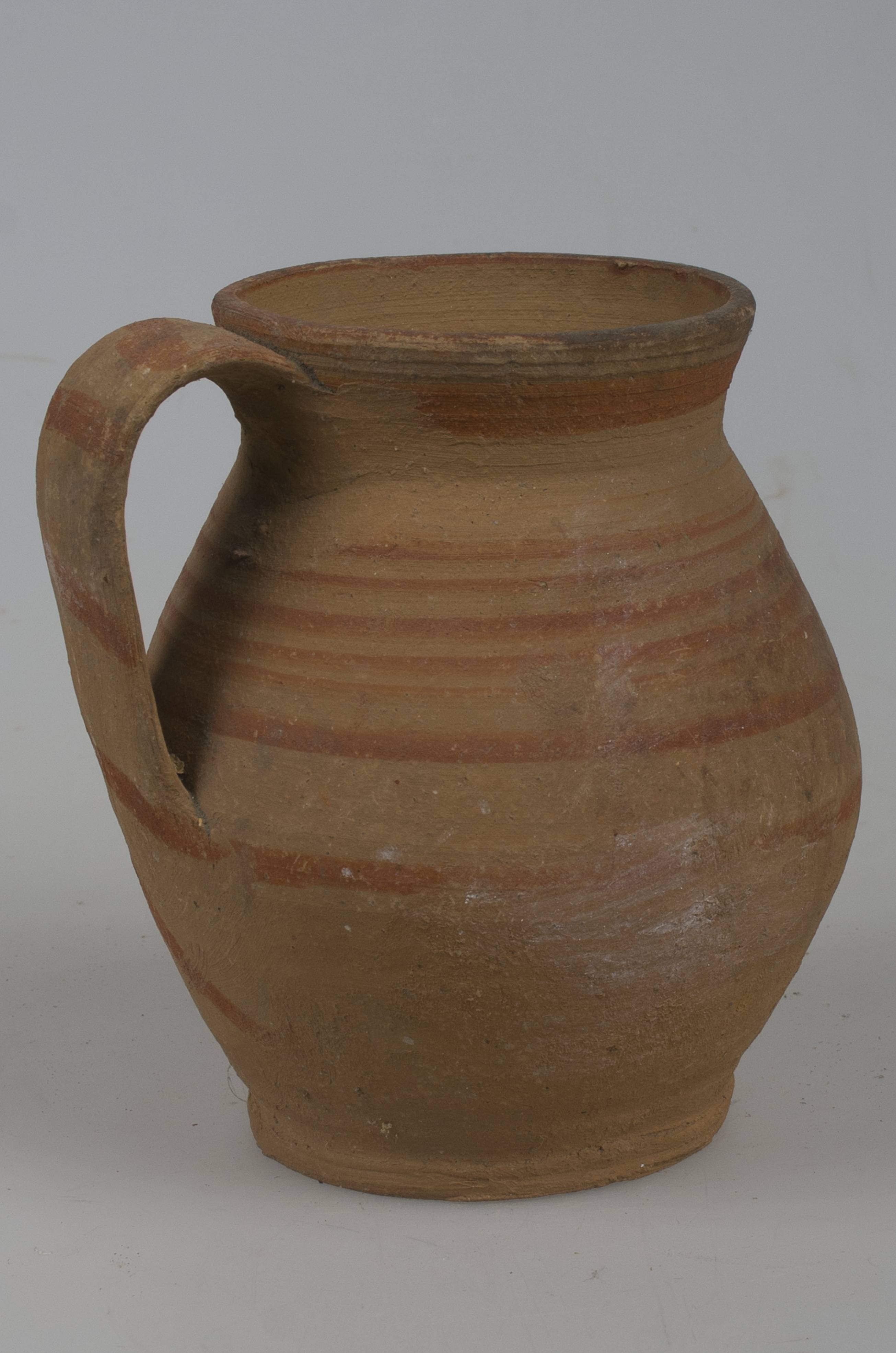 Vas ceramic de formă bitronconică, cu baza dreaptă și plată, având gâtul profilat și buza aproapre dreaptă, pântecele vasului fiind foarte dezvoltat. Piesa prezintă o toartă, care pornește de sub buză și care se unește cu vasul în zona diametrului maxim al acestuia. Corpul nesmălțuit al vasului este decorat în jumătatea superioară cu motive geometrice: linii concentrice decorează umerii și gâtul vasului, toarta fiind ornamentată la rândul ei, cu mai multe linii ușor oblice paralele. Cromatică: fond: maro deschis; motive: roșu.