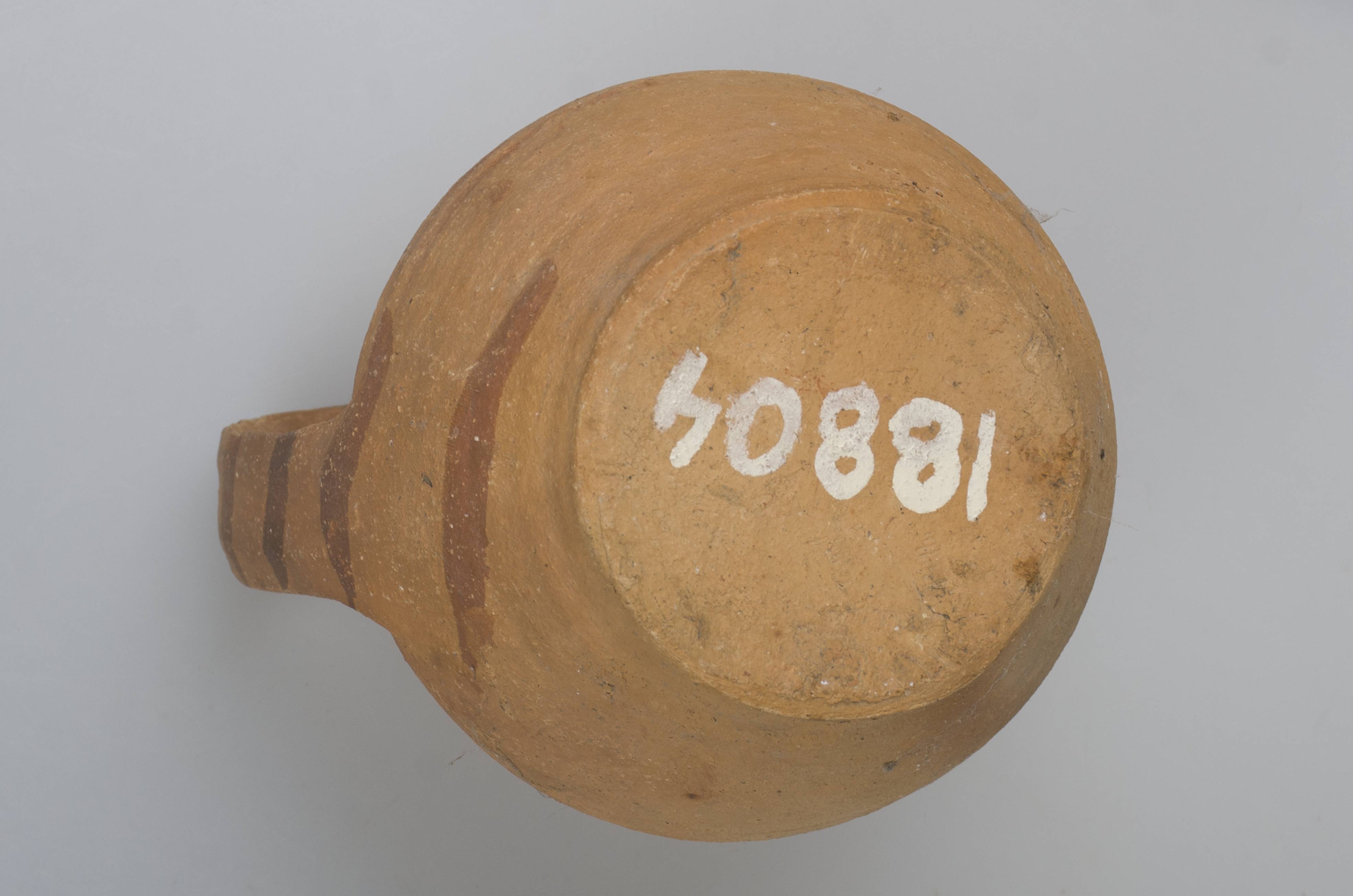 Vas ceramic de formă bitronconică cu baza dreaptă și plată, având gâtul scurt, cu gura largă și buza tăiată drept. Piesa prezintă o toartă, care pornește de sub buză și care se unește cu vasul în zona diametrului maxim al acestuia. Este decorată pe aproape toată suprafața (mai puțin partea inferioară) cu linii drepte mai subțiri și mai late. Toarta este ornamentată cu linii paralele. Vasul este nesmălțuit. Cromatică: fond: cărămiziu; motive: roșu