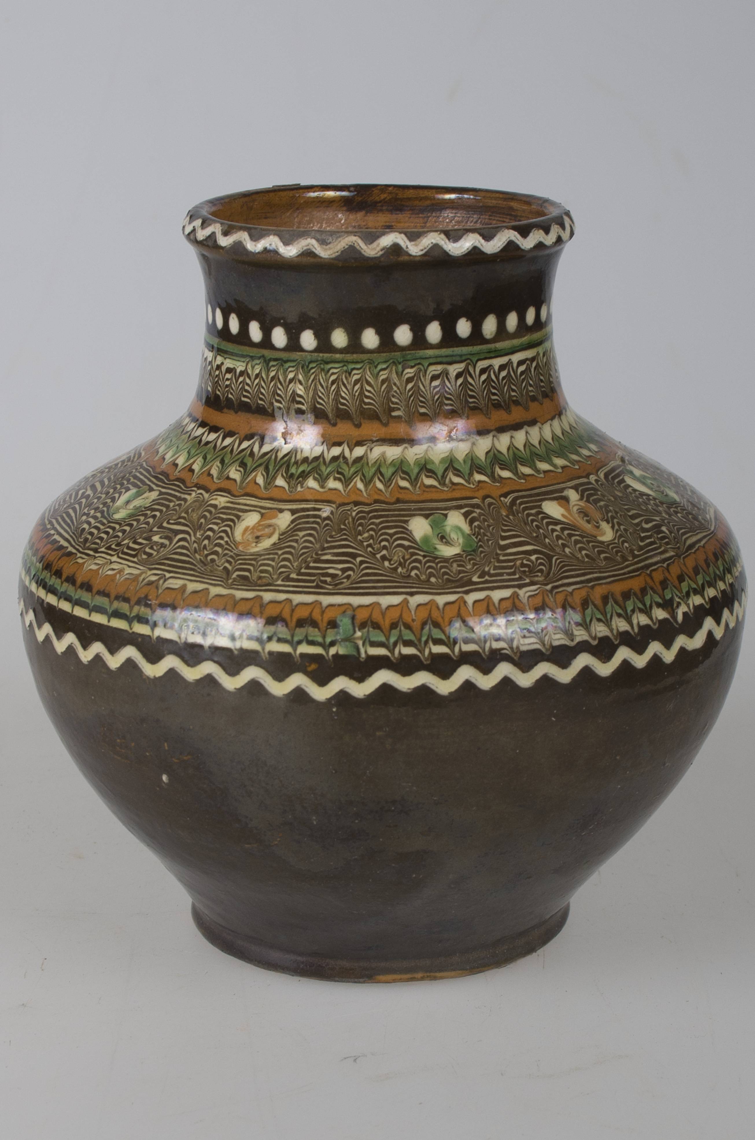 Vas ceramic smălțuit de dimensiuni reduse, realizat la roata olarului, uscat, pictat, ars de două ori și smălțuit. Vaza pentru flori, de formă cilindrică, cu gâtul restrâns și marginile ușor evazate, este „bombată” în zona pântecului. Decorul, realizat la exterior, este compus dintr-un registru realizat cu „gaița” - jirăvit, cuprins între două linii, una în valuri - jos; și una din puncte, sus. Registrul, menționat anterior, este format din decor de tipul „coadei de păun” și un vrej vegetal cu unsprezece „boboci”. Buza vasului a fost și ea decorată cu o linie șerpuită, de culoare albă. Pe fundul vasului a fost redactat cu un obiect ascuțit, textul: „ STELIAN OGREZANU. HUREZ. 1978.”. Cromatica vasului este maro deschis la interior și maro-închis la exterior, iar cea a decorului pictat este maro-închis; maro-roșcat; verde; alb.