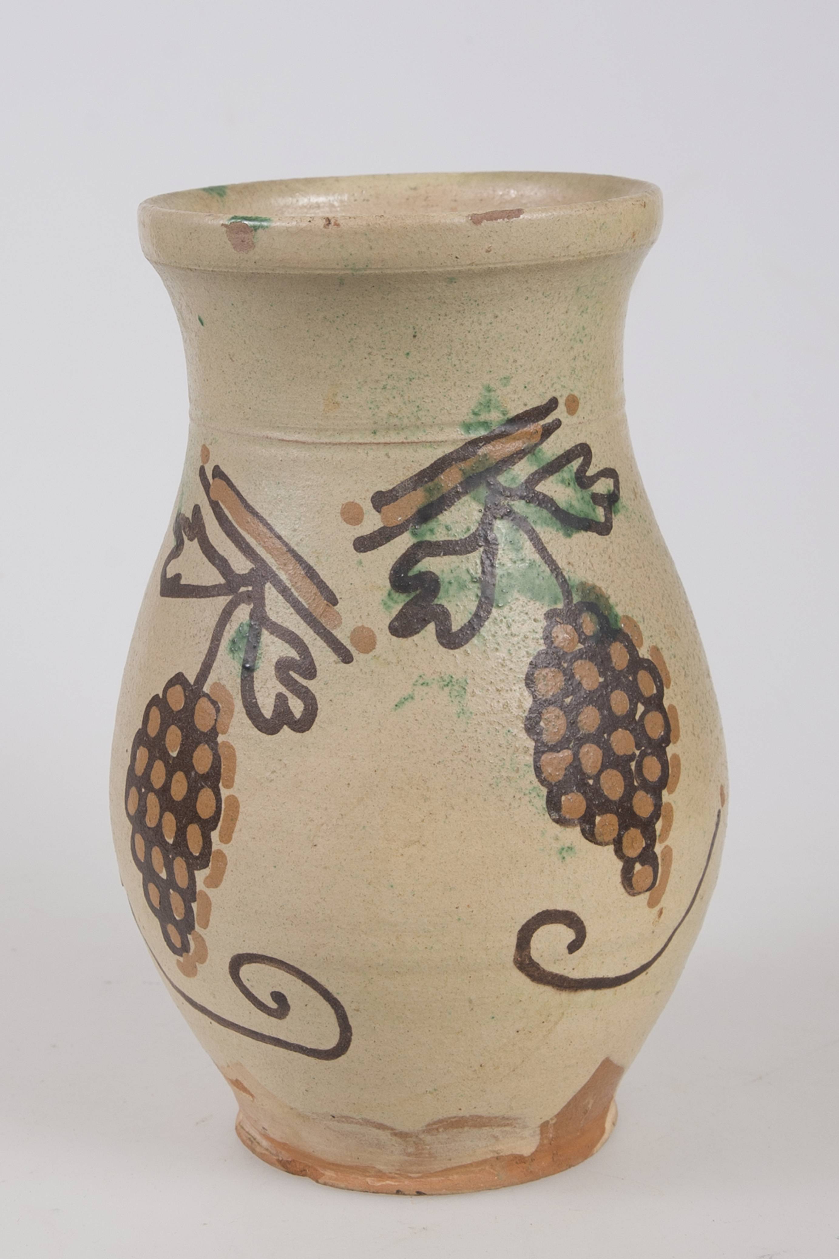 Vas ceramic de formă cilindrică ușor profilat la bază cu gura dreaptă. Buza ușor răsfrântă în exterior cu inel proeminent la bază. Toarta prinsă între mijlocul gâtului și mijlocul vasului. Angobat și smălțuit în interior și exterior. Decor: doi ciorchini de struguri pictați cu cornul; două dungi deasupra torții prin apăsare cu pieptenul. Cromatică: fond: crem; motive: maron; negru; verde.