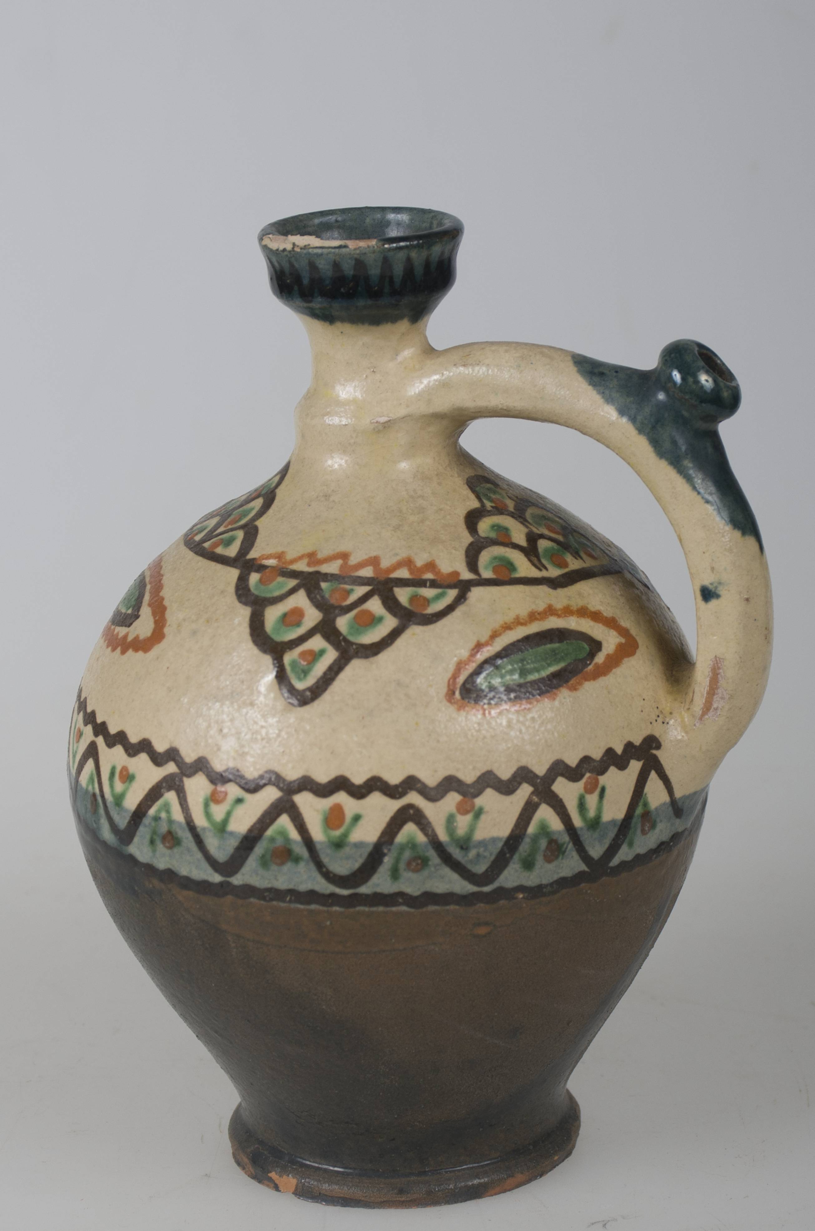 Vas ceramic smălțuit de dimensiuni reduse, modelat la roata olarului, uscat, pictat, ars de două ori și smălțuit. Ulciorașul, de formă cilindrică, cu baza plată și bombat în zona „pântecelui”, are gâtul și gura reduse ca diametru. O toartă pornește dinspre gât, spre diametrul maxim al vasului, având la jumătatea lungimii o „țâță”, care permitea servirea conținutului lichid. Vasul a fost angobat - angobă verde-închis în jumătatea inferioară și angobă gălbuie, în jumătatea inferioară. Peste stratul de angobă gălbuie a fost realizat decorul compus din două linii șerpuite, între care se află o linie în zig-zag, cu colțurile mari. Pe umerii vasului au fost realizate șase triunghiuri din trei rânduri de semicercuri, suprapuse ca solzii, câte unul cu vârful în sus și unul cu vârful în jos. Între triunghiurile orientate cu vârful în jos motive elipsoidale. La gura vasului și „țâță”, recipientul prezintă pete de culoare verzuie. Cromatică: verde; crem; maro-roșcat; brun.