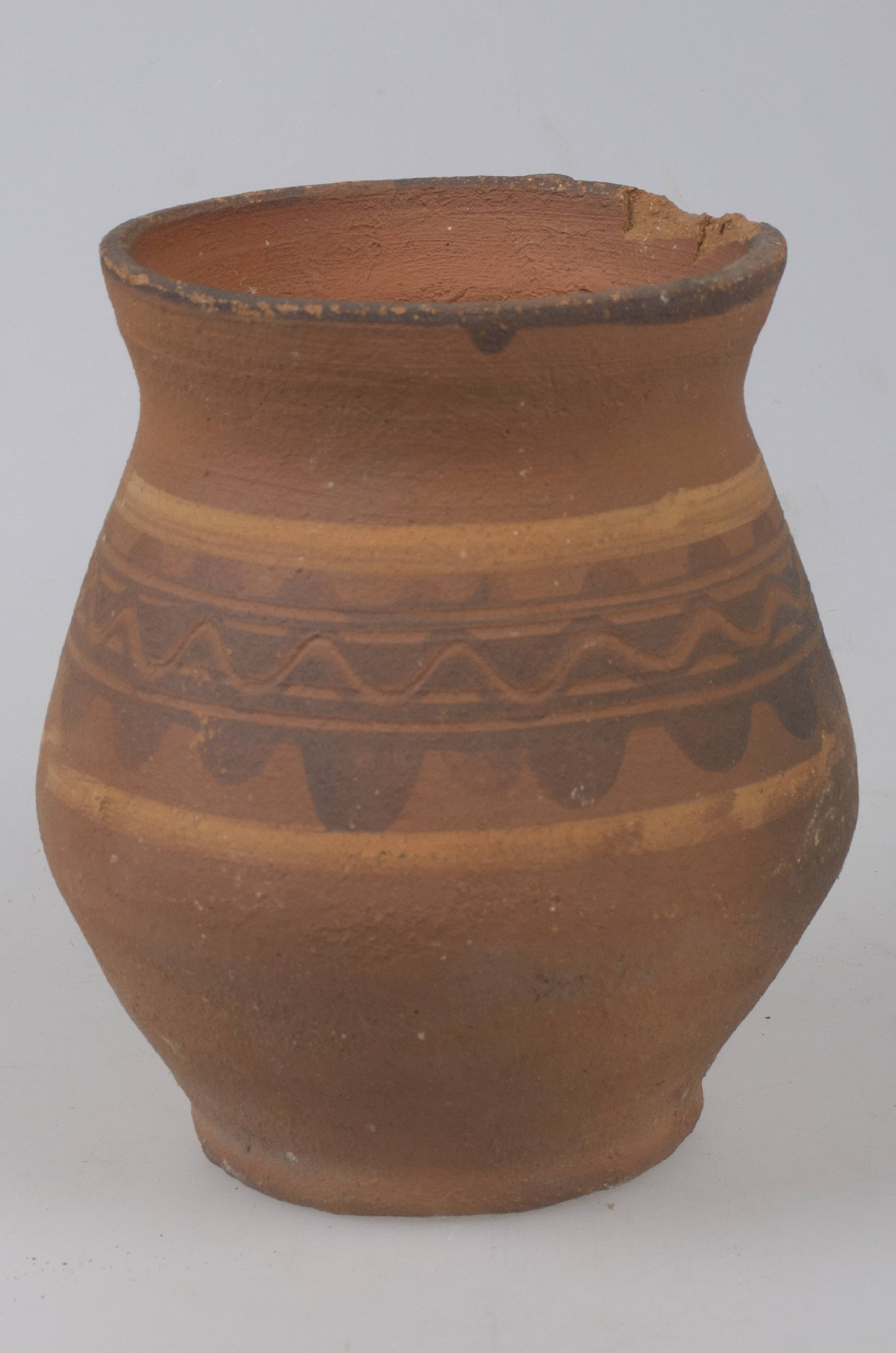 Vas ceramic de formă bitronconică cu baza dreaptă și plată, având gâtul scurt, cu gura largă și buza tăiată drept. Piesa prezintă o toartă, care pornește de sub buză și care se unește cu vasul în zona diametrului maxim situat foarte jos. Vasul este decorat în partea superioară cu motive geometrice: între două linii mai late de culoare albă pictate se găsește o linie în val realizată cu degetul peste care se suprapune o linie subțire în val încadrată de câte o linie dreaptă. Pe toartă sunt pictate mai multe linii orizontale. Buza vasului este pictată cu negru. Vasul este nesmălțuit. Cromatică: fond: cărămiziu; motive: roșu; alb; negru