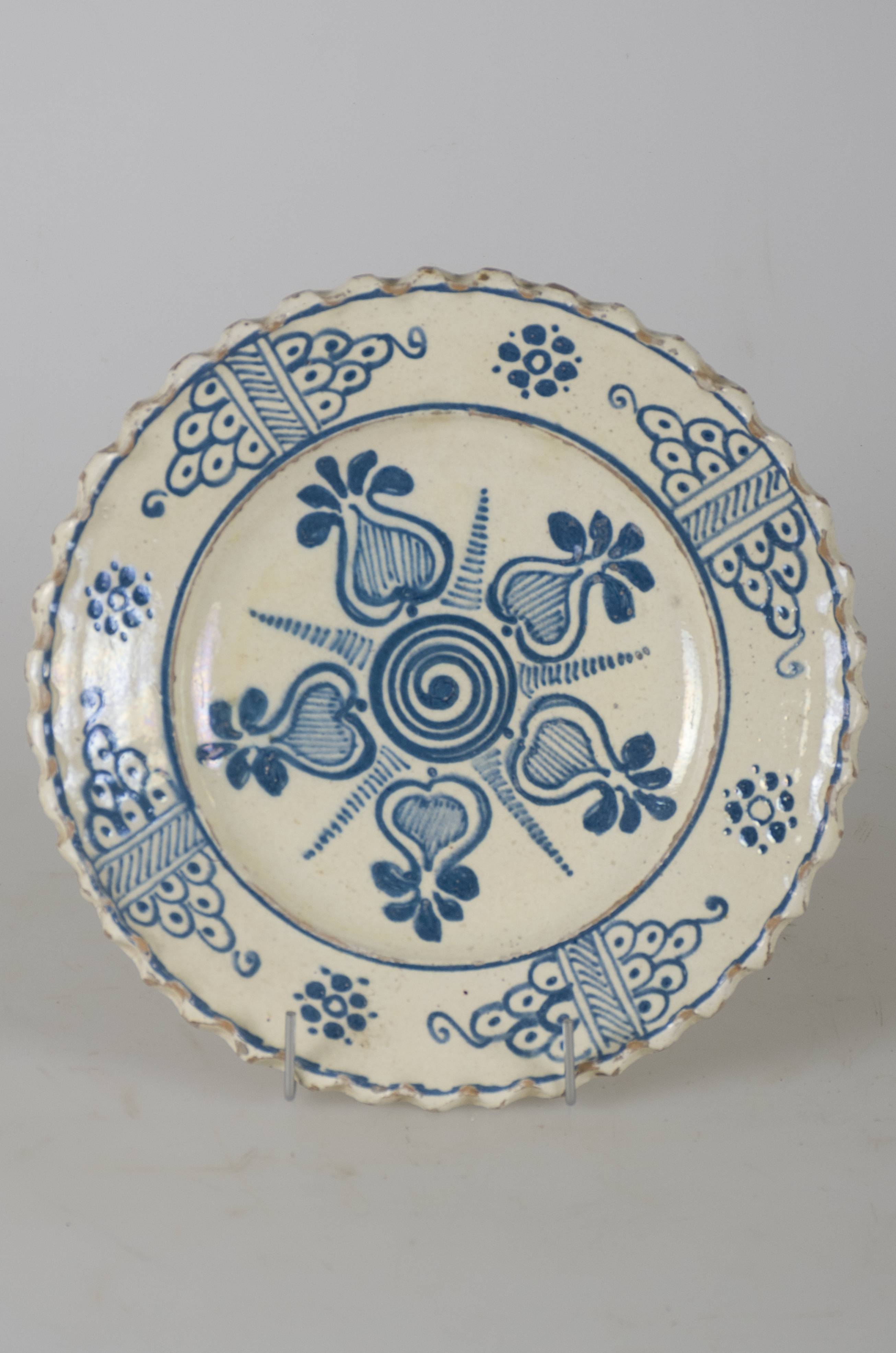 Vas ceramic smălțuit, de formă tronconică, cu marginile puțin ridicate și fundul plat. Pe fond alb avem decorații stilizate în culoarea albastră, înscrisă într-un cerc care conturează fundul vasului, o compoziție ilustrând o floare având în centru un rotund spiralat cu cinci petale în formă de rodie, între ele fiind cinci grupuri de mici linii orizontale care se subțiază spre vârf. Pereții interiori ai vasului împărțiți în patru registre delimitate de hașuri diagonale încadrate de câte două linii verticale. În interiorul registrelor câte o floare compusă din puncte, cercuri și semicercuri cu câte un punct în mijloc simbolizând un ciorchine de struguri cu vrej în vârf. Buza vasului este ondulată. Prezintă două orificii, la bază, pe partea din spate, pentru a fi suspendată. Cromatică: fond: alb; motive: albastru.