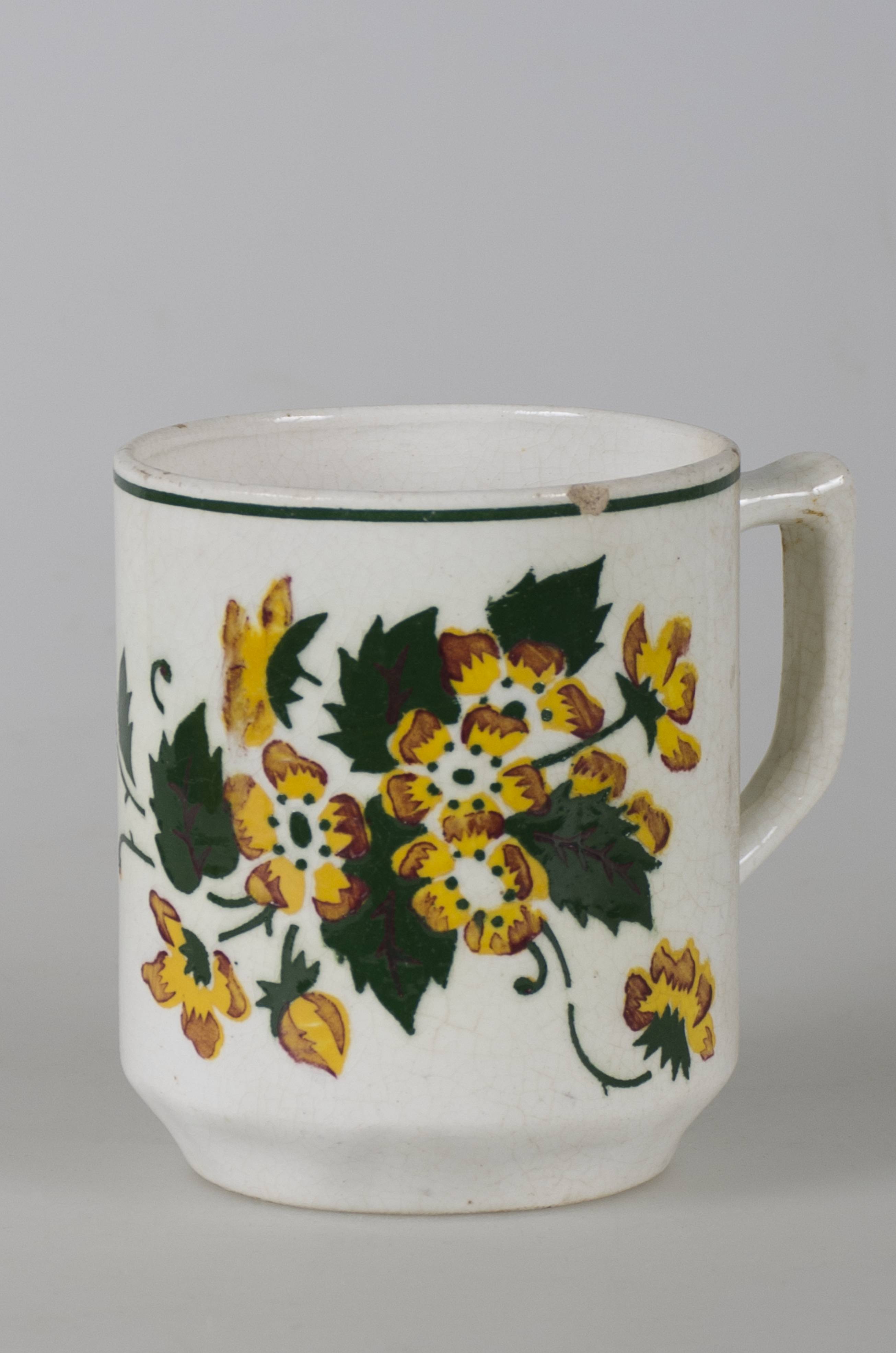 Recipient smălțuit de formă cilindrică. Pe fond alb prezintă decorații în registru floral-vegetal ilustrând flori cu petale galbene-maro, împreună cu tulpini și frunze verzi. Prezintă o toartă trapezoidală ce unește gura cu treimea inferioară. Gura cănii este conturată de o linie circulară verde.