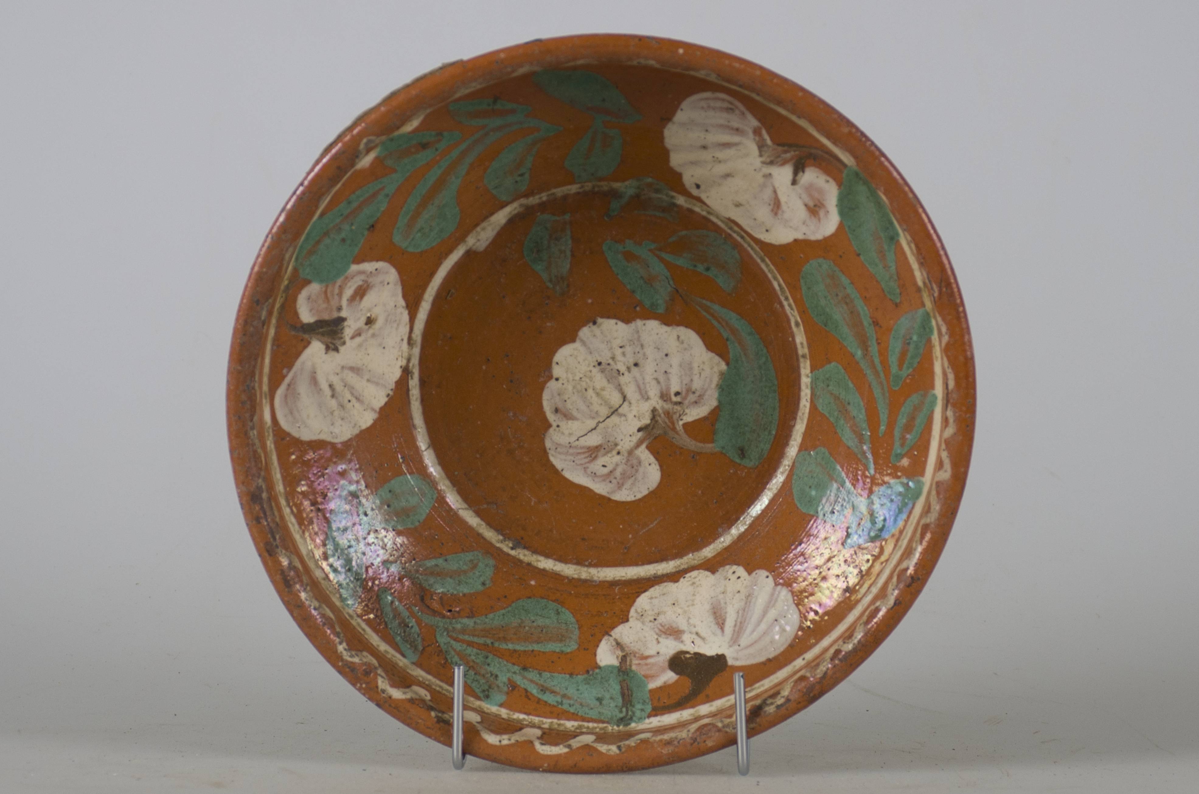Vas ceramic smălțuit în interior, de formă tronconică, cu marginile puțin ridicate și fund plat. Pe fond maro deschis avem decorații realizate prin pictare cu pensula, în registru floral-vegetal ilustrând patru flori albe cu frunze verzi, una dintre flori se află pe fundul vasului, celelalte trei dispuse circular pe pereții interiori ai vasului fiind despărțite de frunze verzi. Marginile farfuriei sunt conturate de două linii albe dispuse circular, cea din partea superioară fiind ondulată. O altă linie circulară albă conturează fundul vasului. Pe spate, la bază, prezintă două perforații pentru suspendare. Cromatică: fond: maro; motive: alb; verde.