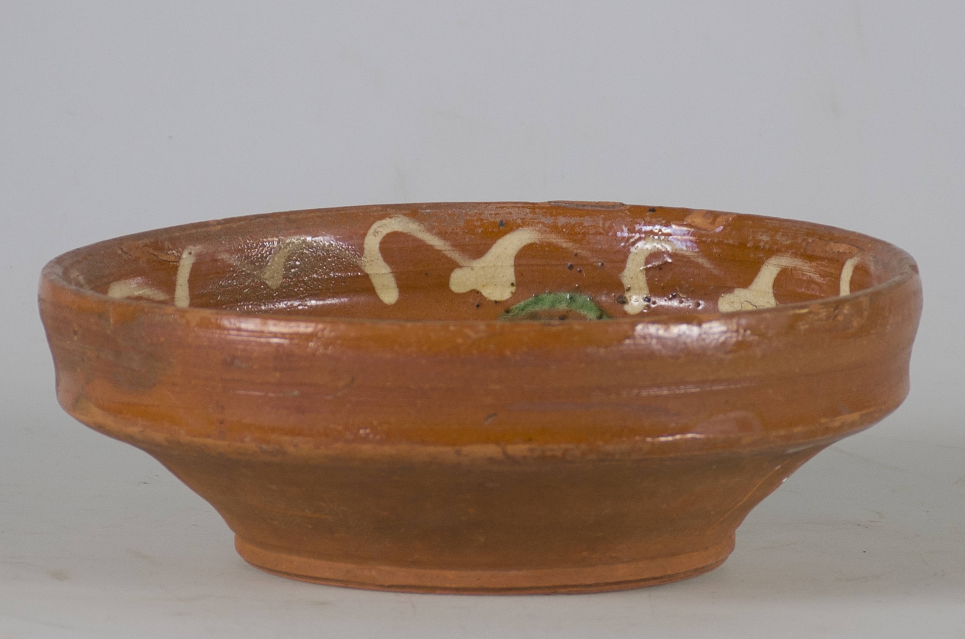 Vas ceramic smălțuit în interior, de formă tronconică, cu marginile puțin ridicate și fundul plat. Pe fond maro deschis decorații realizate prin pictare cu pensula, ilustrând patru flori cu petale albe, frunze verzi și tulpini negre. Una dintre flori se află pe fundul vasului, celelalte trei sunt dispuse circular pe pereții interiori ai vasului despărțite de frunze. Pe marginea farfuriei linie ondulată albă. Pe spate, la bază, două orificii pentru suspendare/prindere. Cromatică: fond: maro; motive: alb; verde; negru