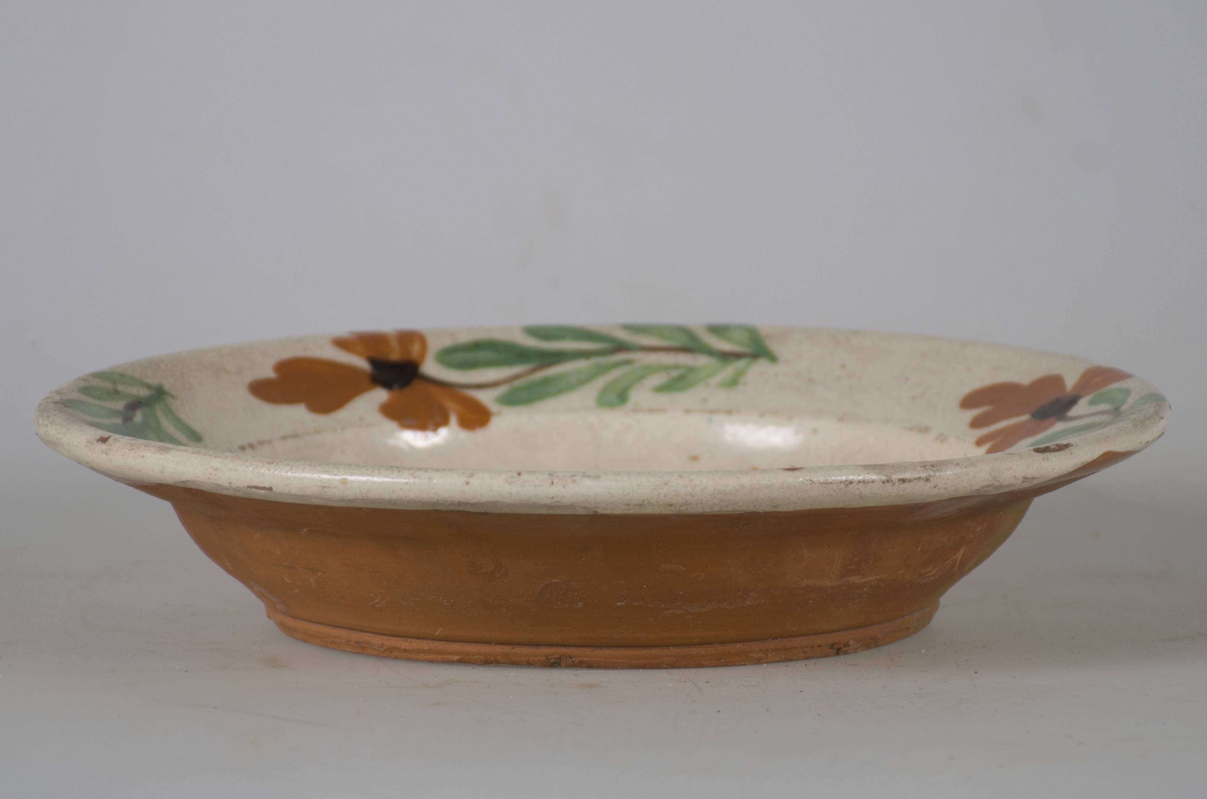 Vas ceramic smălțuit, de formă tronconică, cu marginile puțin ridicate și fundul plat. Pe fond alb prezintă patru flori (două cărămizii și două albastre dispuse în careu), separate de frunze verzi. Pe marginile vasului sunt dispuse circular patru flori cărămizii. Fiecare floare are tulpina neagră și câte un punct negru. Pe spate, la bază, prezintă o perforație pentru a fi suspendată. Cromatică: fond: alb; motive: cărămiziu; albastru; verde; negru.