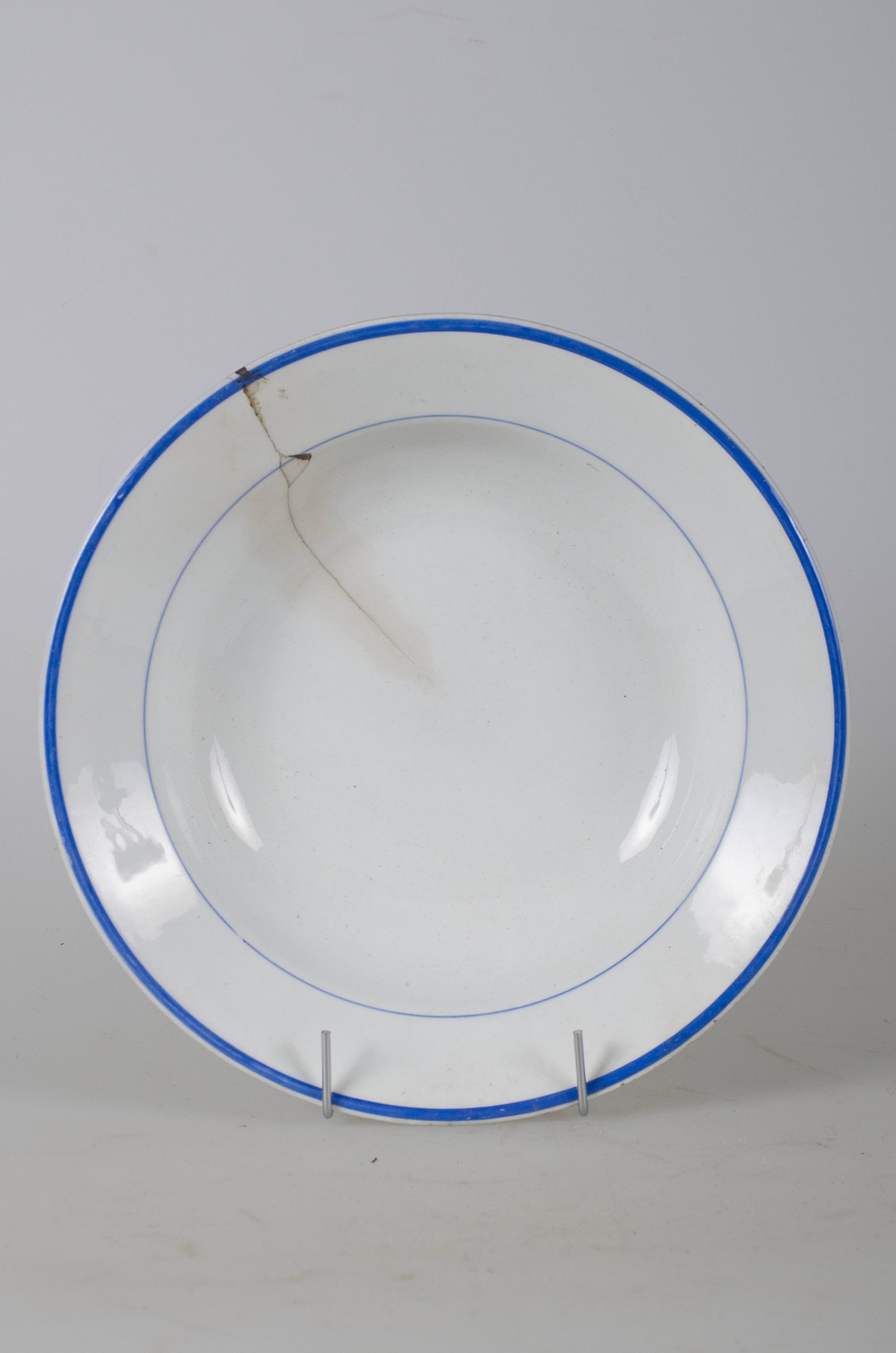 Vas ceramic smălțuit, de formă tronconică, cu marginile puțin ridicate și fundul plat. Farfuria este albă. Marginile vasului sunt încadrate de două linii albastre dintre care una mai subțire și cea care conturează buza mai groasă. Cromatică: fond: alb; motive: albastru.