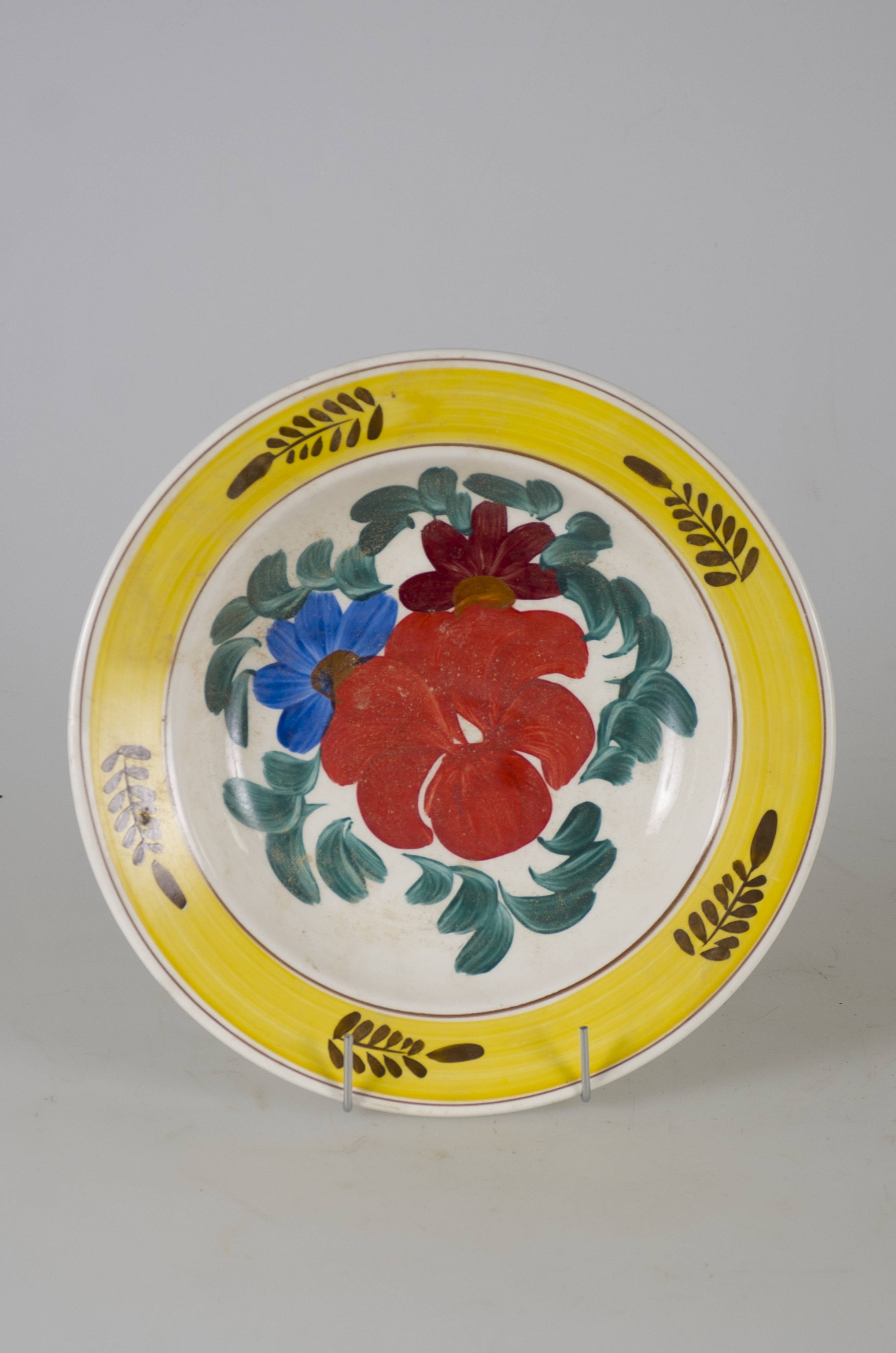 Vas ceramic smălțuit, de formă tronconică, cu marginile puțin ridicate și fundul plat. Pe mijloc sunt decorații în registru floral-vegetal, ilustrând trei flori: una cu petale roșii de mai mari dimensiuni și două mai mici având fiecare petale albastre și mov. Compoziția aflată pe fundul vasului este mărginită de frunze verzi. Pe marginile vasului este dispusă o bandă galbenă peste care sunt prezente, circular, cinci crengi cu frunze maro. Marginile sunt conturate cu două linii maro. Prezintă două orificii, la bază, pe partea din spate, pentru a fi suspendată.