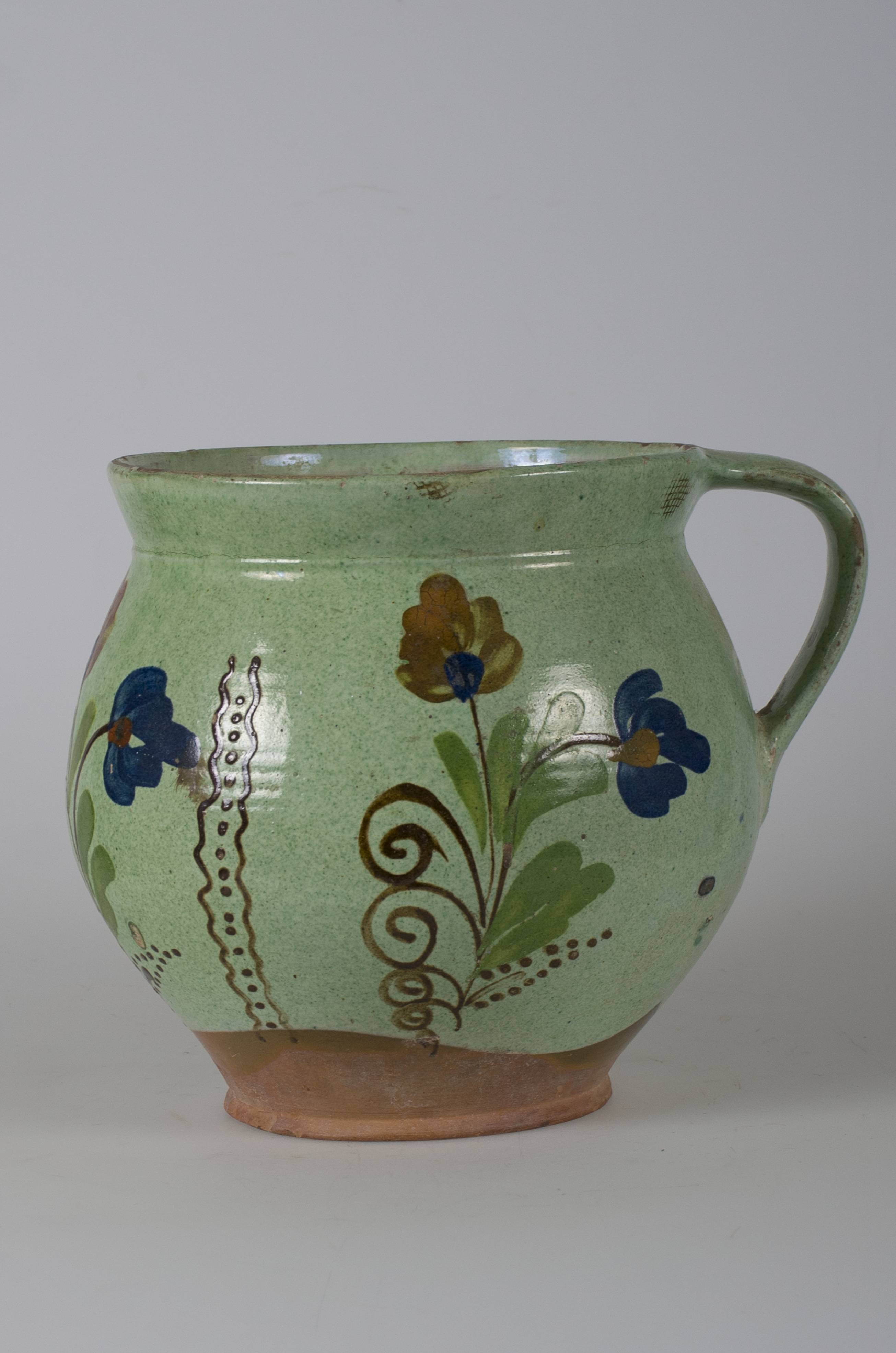 Vas ceramic smălțuit, de formă bitronconică, bombat în partea mediană și marginile evazate spre exterior. Pe fond verde deschis decorații realizate prin pictare cu pensula, în registru floral-vegetal. Trei registre delimitate de câte două linii ondulate duble cu șir de puncte maro. În fiecare registru câte două flori cu petale albastre și roșii, tulpini maro și frunze verzi. Prezintă o toartă ce unește gura vasului cu partea mediană. În marginea oalei, partea opusă toartei incizate literele EK. La baza toartei incizate literele EE. Cromatică: fond: verde deschis; motive: albastru; verde; maro; roșu.