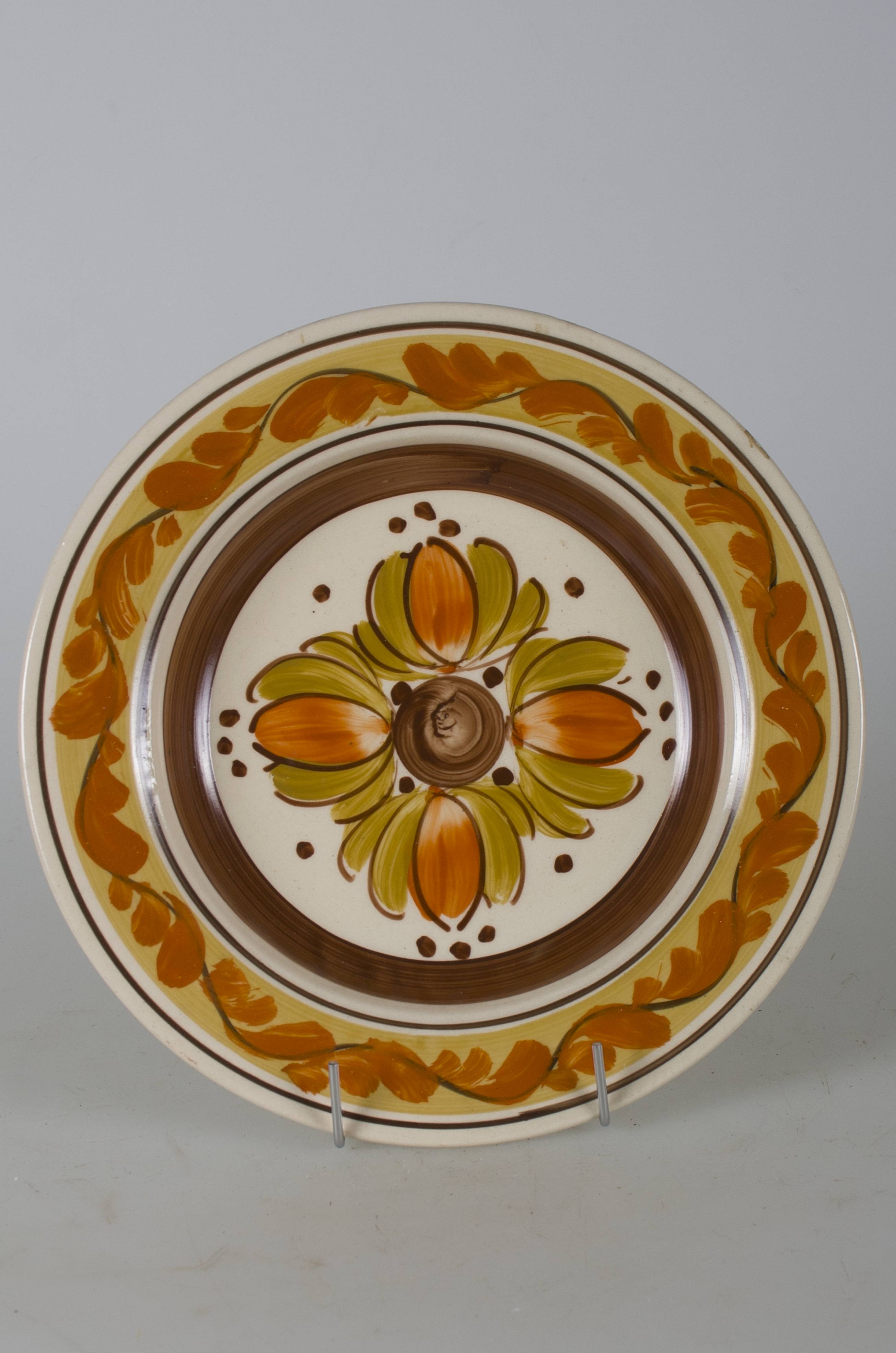 Vas ceramic smălțuit, de formă tronconică, cu marginile puțin ridicate și fund plat. Pe fond alb avem decorații în registru floral-vegetal. Pe fundul vasului o compoziție având în centru un cerc plin maro din care radiază patru flori (bujori) cu petalele din mijloc portocalii și celelalte petale verzi. Compoziția este completată de puncte maro grupate câte trei sau individual. Pereții interiori ai vasului conturați de o bandă maro. Pe marginile farfuriei pe fond gălbui este dispusă o linie ondulată circulară dublată de frunze portocalii. Marginile conturate de două linii maro dispuse circular. Pe spate, la bază, prezintă o perforație pentru suspendare. Cromatică: fond: alb; motive: maro; portocaliu; verde; galben.