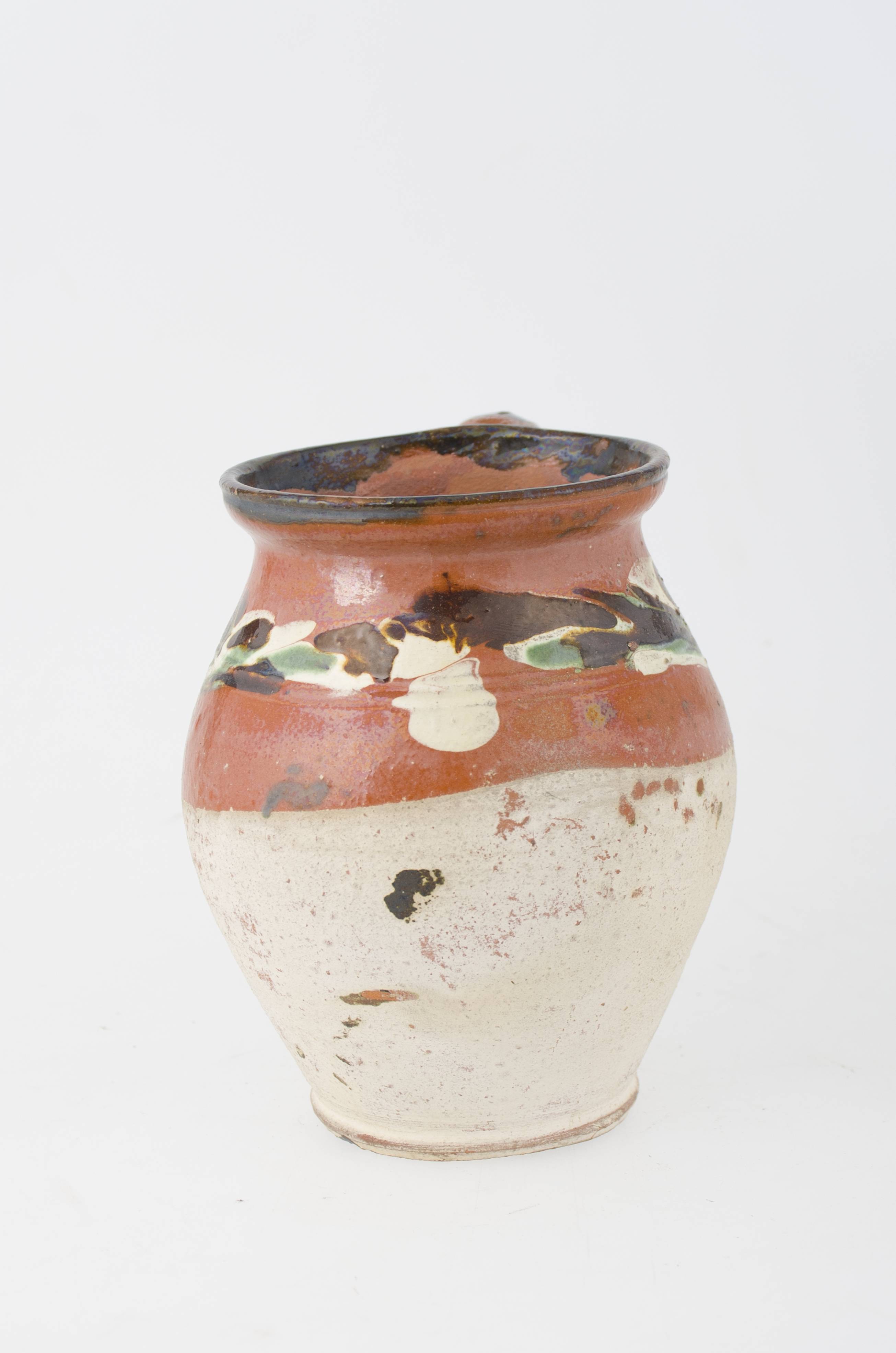 Vas ceramic de formă bitronconică, rotunjită cu baza mică, corpul bombat la mijloc, gâtul larg și gura evazată, ușor concavă. O toartă îngustă și plată pornește drept din buză și coboară în mijlocul pântecelui, arcuindu-se într-un unghi larg și ascuțit. Partea superioară dată cu "rușală", cu vargă încizată și pete scurse: albe, brun și verde, și smalț incolor translucid, partea inferioară angobată și nesmălțuită.