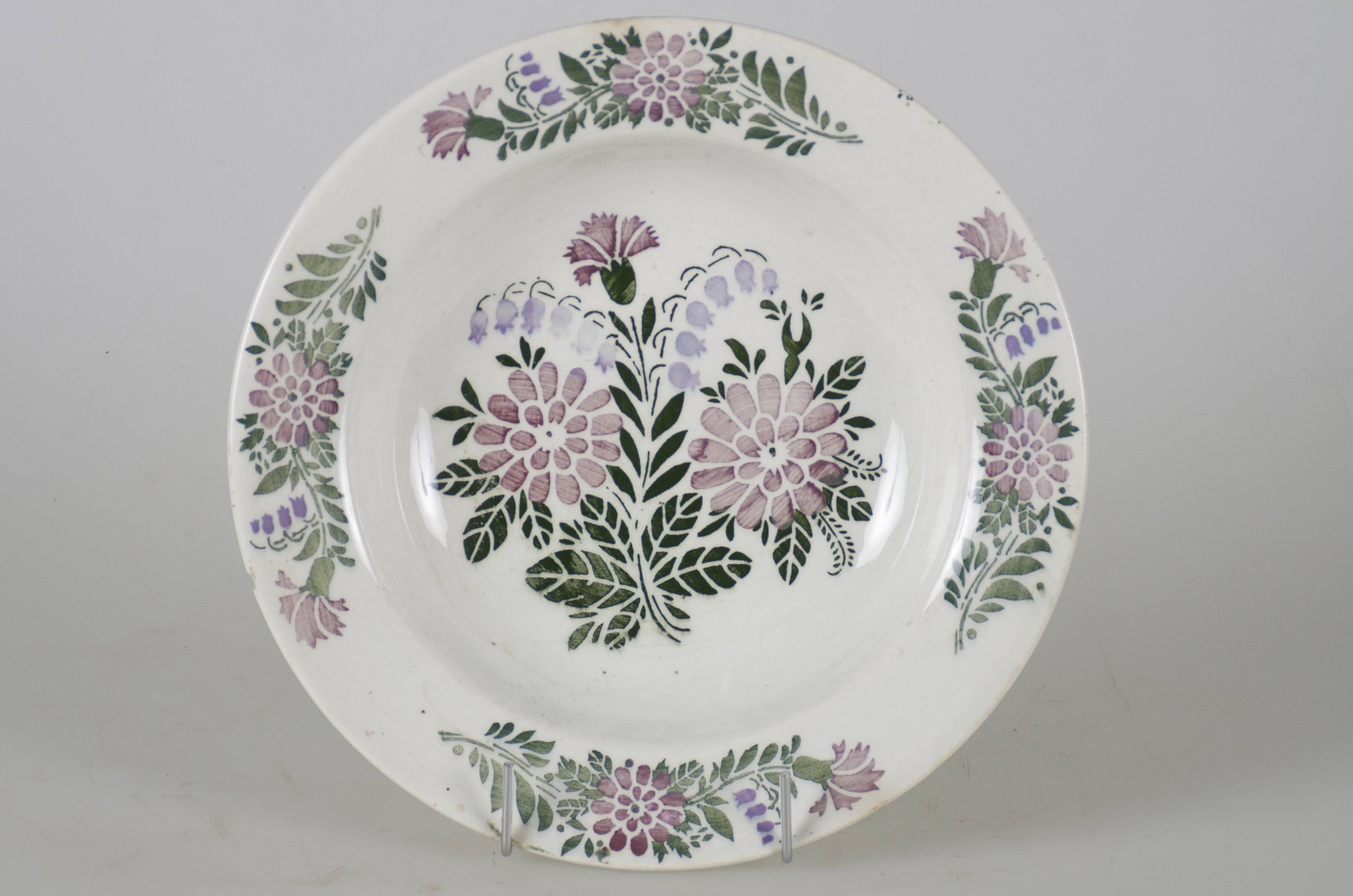 Vas ceramic smălțuit, de formă tronconică, cu marginile puțin ridicate și fundul plat. Pe fond alb prezintă decorații ilustrând flori roșii (crizanteme) și albastre (clopoței) împreună cu frunze verzi. Pe fund, este o compoziție cu două crizanteme și două lăcrămioare având în partea superioară o garoafă văzută din profil, împreună cu frunze. Pe marginile vasului se dispun patru registre similare cu cea de pe fundul farfuriei, având numai câte o floare din fiecare tip. Pe spate, la bază, prezintă o perforație pentru suspendare. Cromatică: fond: alb; motive: roșu; verde; albastru.