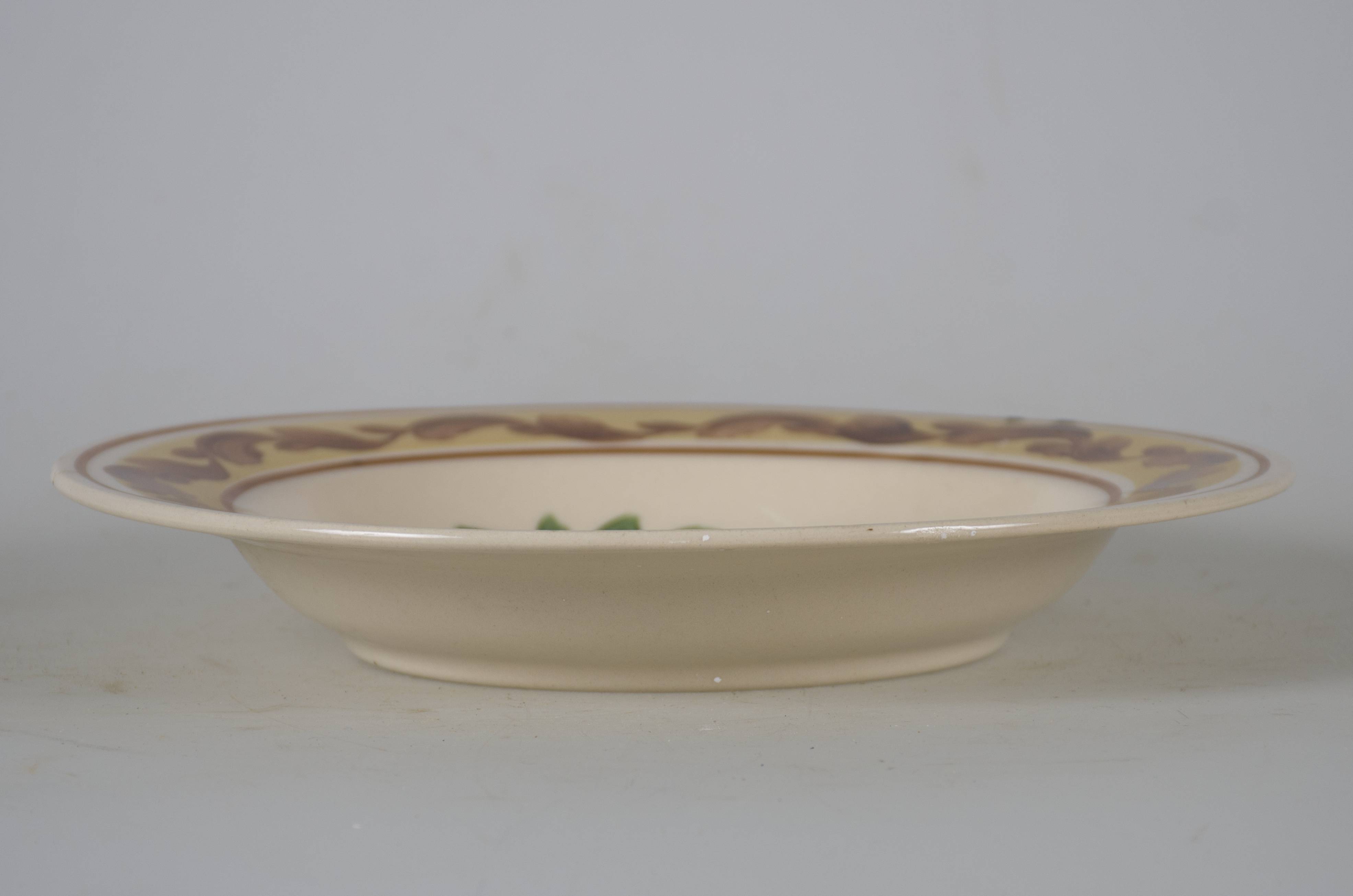 Vas ceramic smălțuit, de formă tronconică, cu marginile puțin ridicate și fund plat. Pe fond alb sunt decorații realizate prin pictare cu pensula în registru floral-vegetal, ilustrând o compoziție de trei flori fiecare cu petale portocalii, albastre și maro. Compoziția este încadrată de frunze verzi. Pe marginea farfuriei este dispusă o bandă bej pe care se suprapun decorații sub formă de șir de frunze maro sub formă de ondulație. Acestea sunt mărginite de două linii maro dispuse circular. Pe spate, la bază, prezintă o perforație pentru suspendare. Cromatică: fond: alb; motive: portocaliu, albastru; maro; verde; bej.