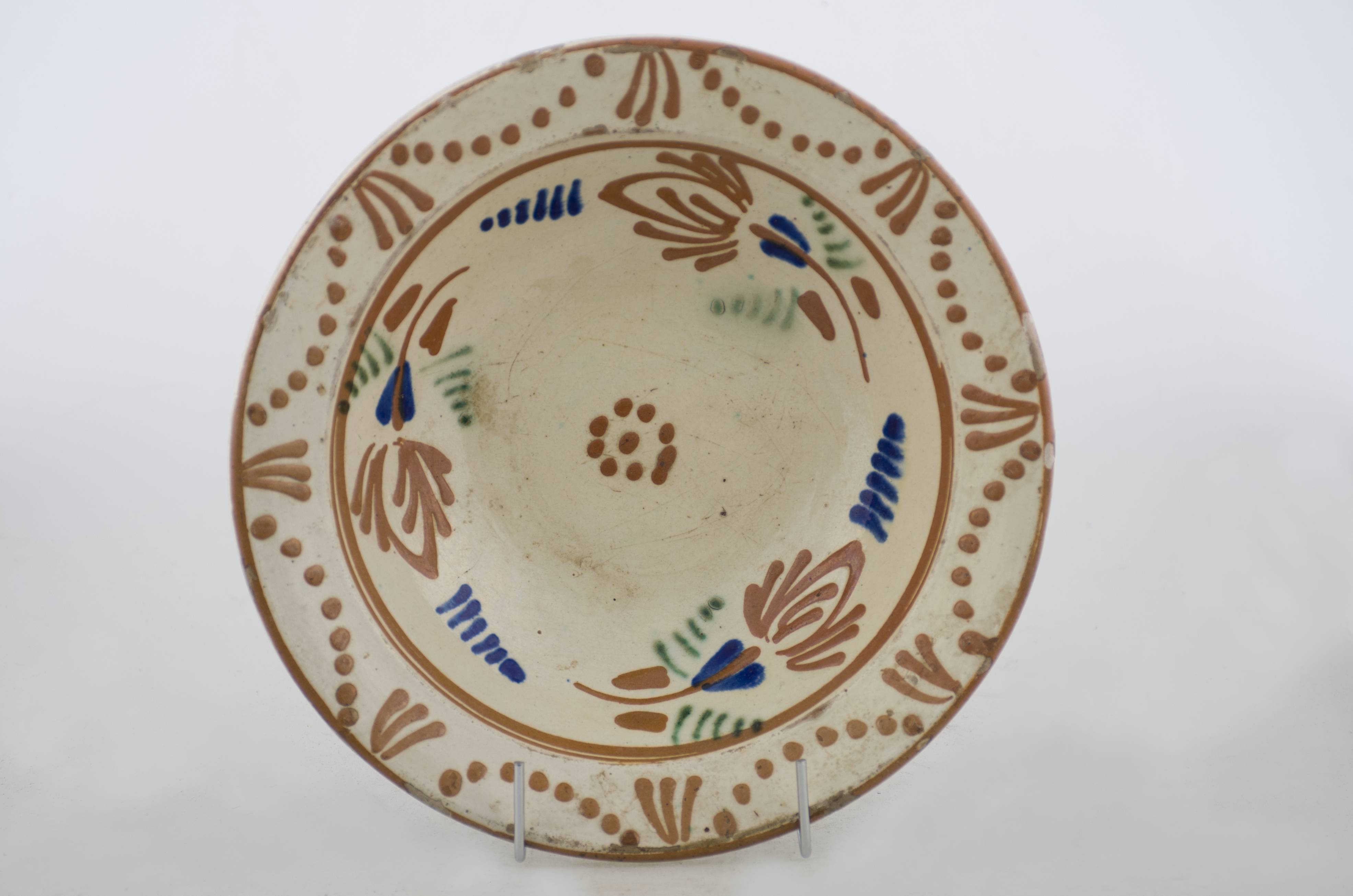 Vas ceramic de formă tronconică cu baza plată, pereții larg evazați și buza profilată. După modelarea la roată, uscarea și arderea recipientului, a fost aplicat un strat de angobă în interiorul vasului, peste care a fost pictat decorul floral și vegetal stilizat, format din trei registre. În primul registru, situat pe fundul vasului, au fost realizate zece puncte, care compun o floare cu nouă petale, cel de-al zecelea punct fiind plasat central. Al doilea registru, cel care decorează pereții recipientului ceramic și este mărginit de o linie circulară, a fost decorat cu motive florale stilizate: trei flori mari, cu frunze, ce sunt despărțite de câte o frunză de culoare albastru, realizată la rândul ei din câte șase linii paralele. Cel de-al treilea registru, a fost ornamentat cu opt flori cu câte trei petale, despărțite de alte opt linii semicirculare, formate din câte opt puncte. Cromatică: fond: alb; motive: verde; albastru; maro-roșcat.