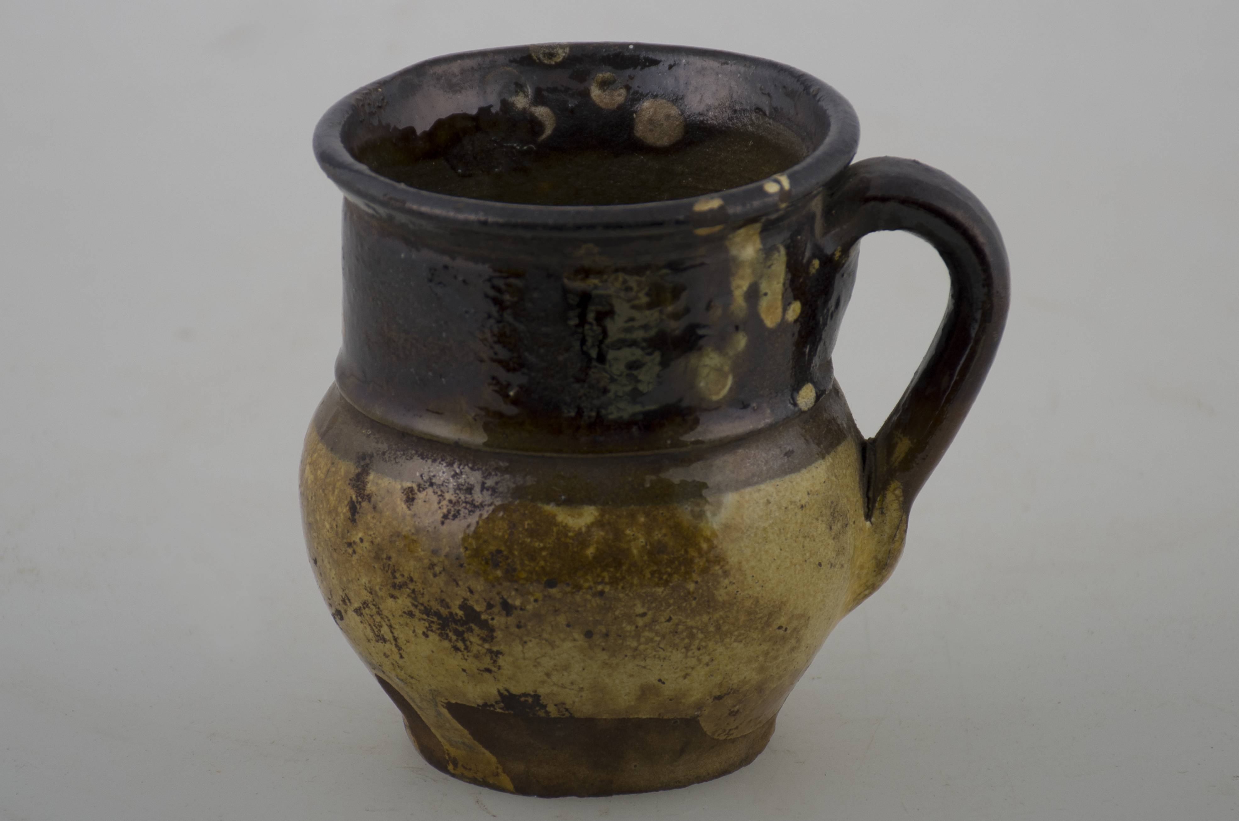 Recipient ceramic de mici dimensiuni, cu baza plată, corpul ușor bombat, gât foarte înalt și buza evazată. Prezintă o toartă care pornește de sub buză și se unește cu corpul în zona diametrului maxim. Partea inferioară este pictată în culoare galben, iar partea superioară pictată în culoarea maro închis cu câteva pete de culoare galbenă. Cromatică: galben; maro închis.