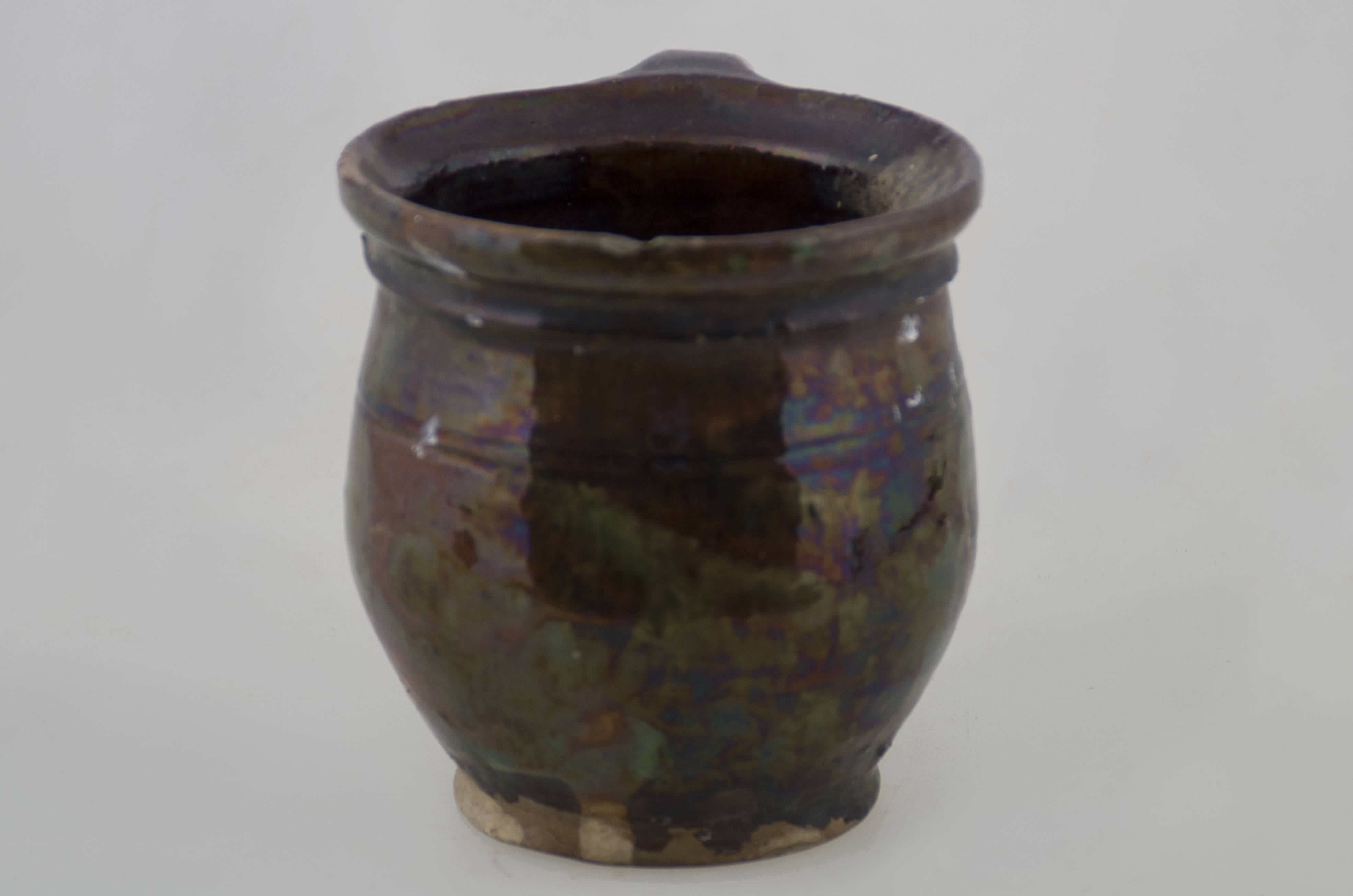 Recipient ceramic bitronconic, de mici dimensiuni, cu baza plată, corpul bombat, pereții ușor invazați spre gură, cu gât scurt și cu inel, cu buza evazată și ușor înălțată. Prezintă o toartă care pornește din buza vasului și se unește cu corpul sub diametrul maxim. Este smălțuit în interior și la exterior. Piesa este decorată cu un brâu din două linii orizontale incizate. Cromatică: fond maro; pete verzi.