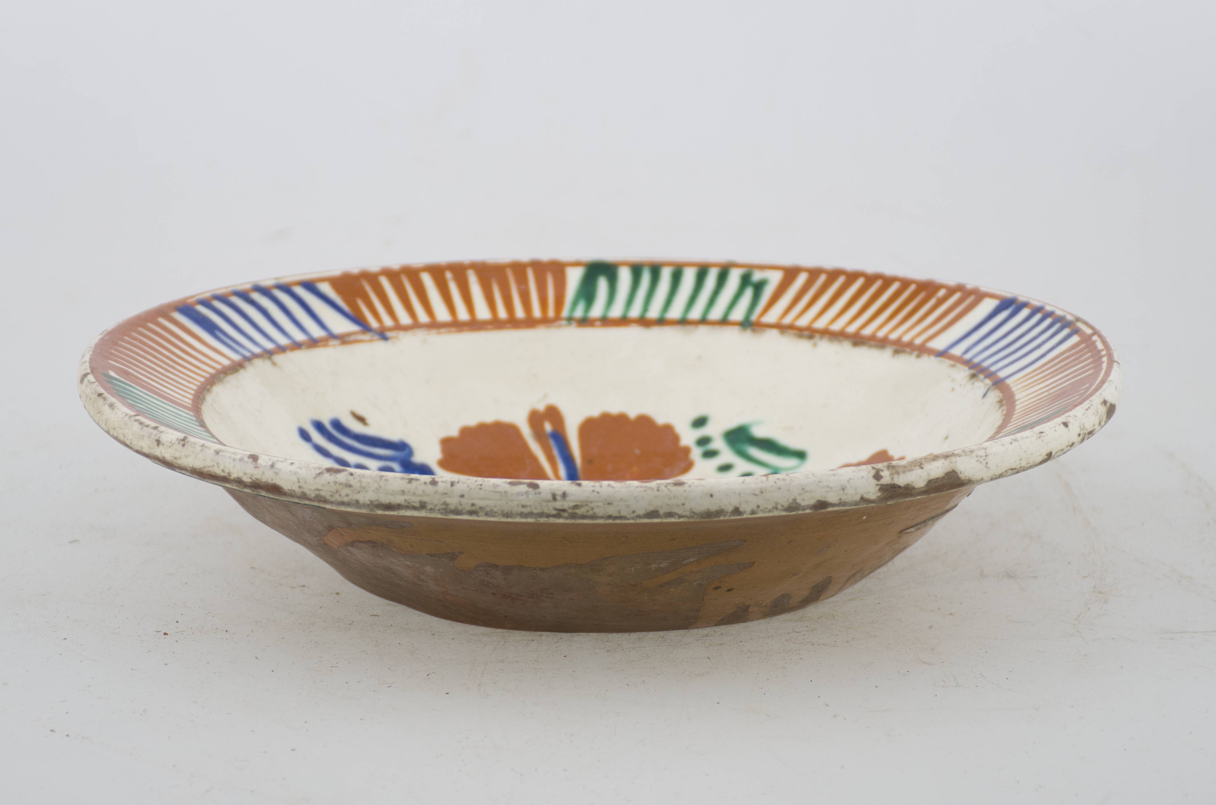 Vas ceramic de formă tronconică cu baza plată, pereții larg evazați și buza profilată. După modelarea la roată, uscarea și arderea recipientului, a fost aplicat un strat de angobă în interiorul vasului, peste care a fost pictat decorul floral și vegetal stilizat, format din două registre. În primul registru, situat pe fundul vasului și încadrat de o linie circulară, au fost realizate patru flori, cu petale maro-roșcate, în jurul cărora se regăsesc frunze verzi și albastre. Cel de-al doilea registru, cel care decorează buza vasului și este mărginit de o linie circulară, a fost decorat cu grupuri de linii verticale paralele succesive, de diferite culori. Cromatică: crem la interior; cărămiziu la exterior; motive: verde; albastru; maro-roșcat. Prezintă uzură funcțională.