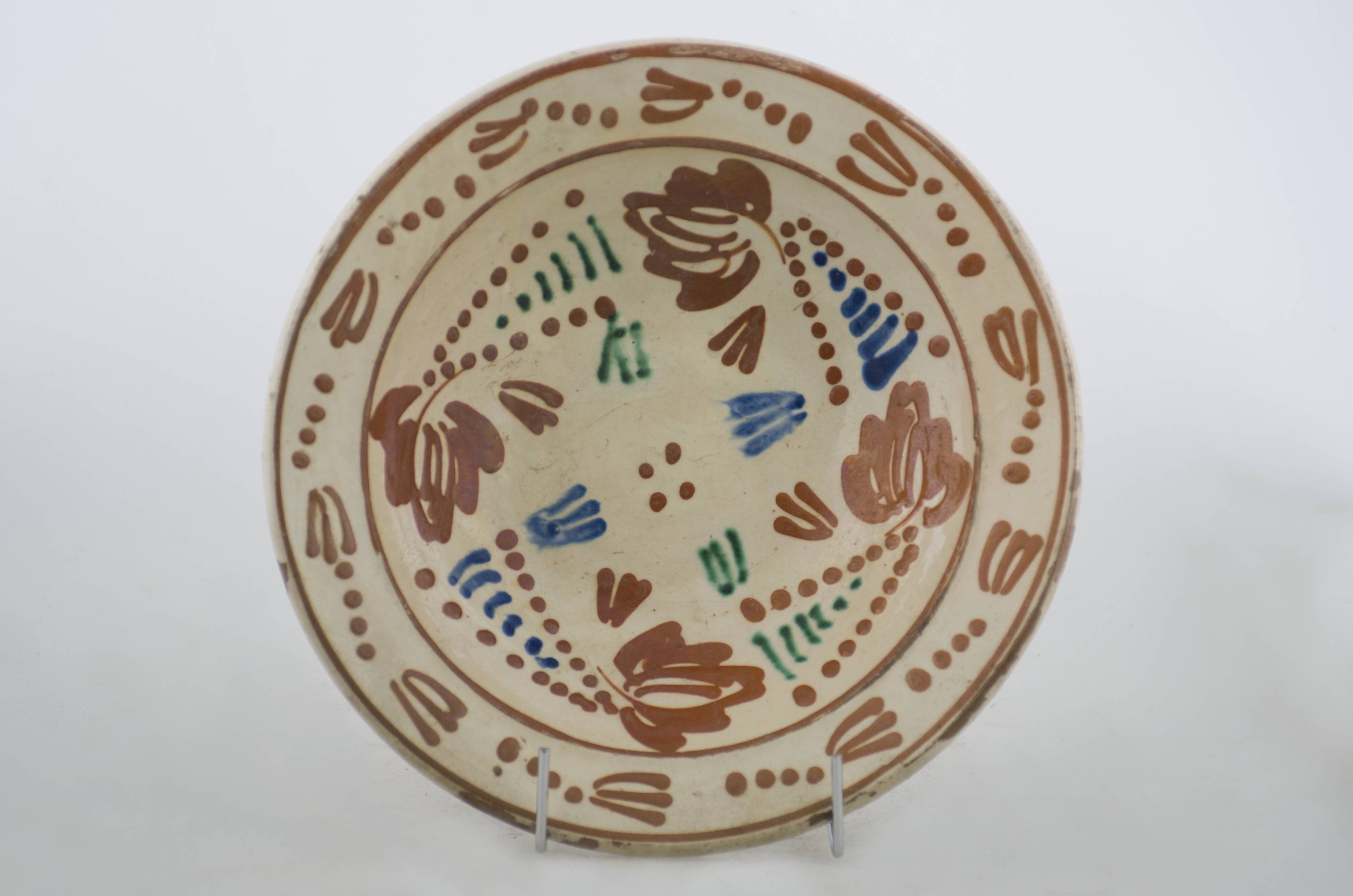 Vas ceramic de formă tronconică, cu baza plată, pereții larg evazați și buza profilată. După modelarea la roată, uscarea și arderea recipientului, a fost aplicat un strat de angobă în interiorul vasului, peste care a fost pictat decorul floral și vegetal stilizat, format din două registre mărginite de câte un cerc. Pe fundul vasului au fost realizate patru puncte, în jurul cărora se regăsesc opt petale, pe pereții evazați fiind pictate patru motive florale stilizate circulare. Zece flori, cu tulpina formată din patru puncte, compun cel de-al doilea registru pictural, cel care decorează buza blidului ceramic. Cromatică: fond: crem; motive: verde; maro-roșcat; albastru.