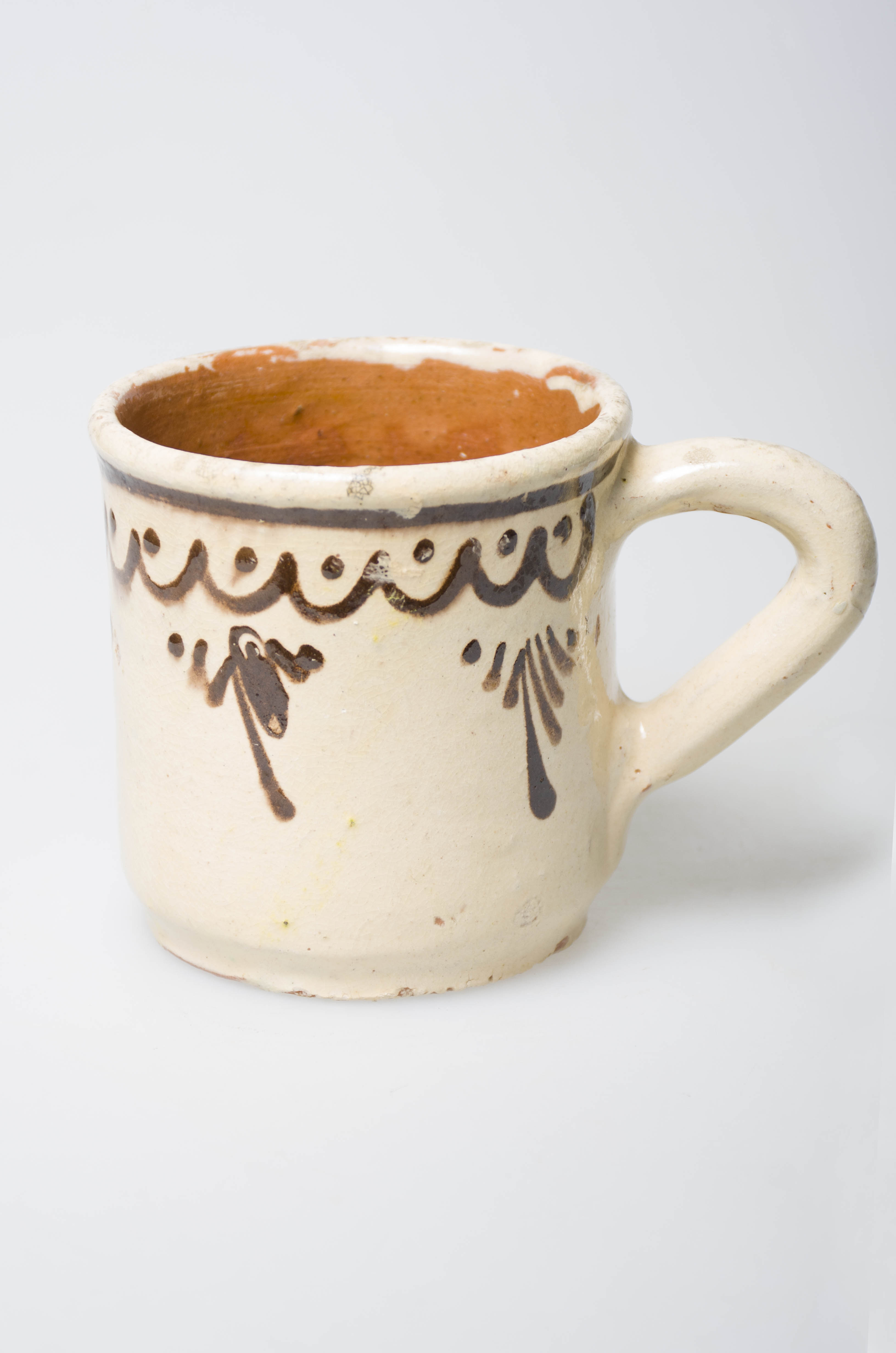 Ceașca este confecționată din ceramică, având forma cilindrică. Aceasta este prevăzută cu o toartă mare. Decorul este pictat: sub buza există o linie ondulată pe care sunt dispuse trei semicercuri cu câte un punct în fiecare buclă. Pe corpul cănii există cinci grupe de linii verticale dispuse în formă triunghiulară. Cromatică: fondul este alb, iar motivele sunt pictate cu maro.