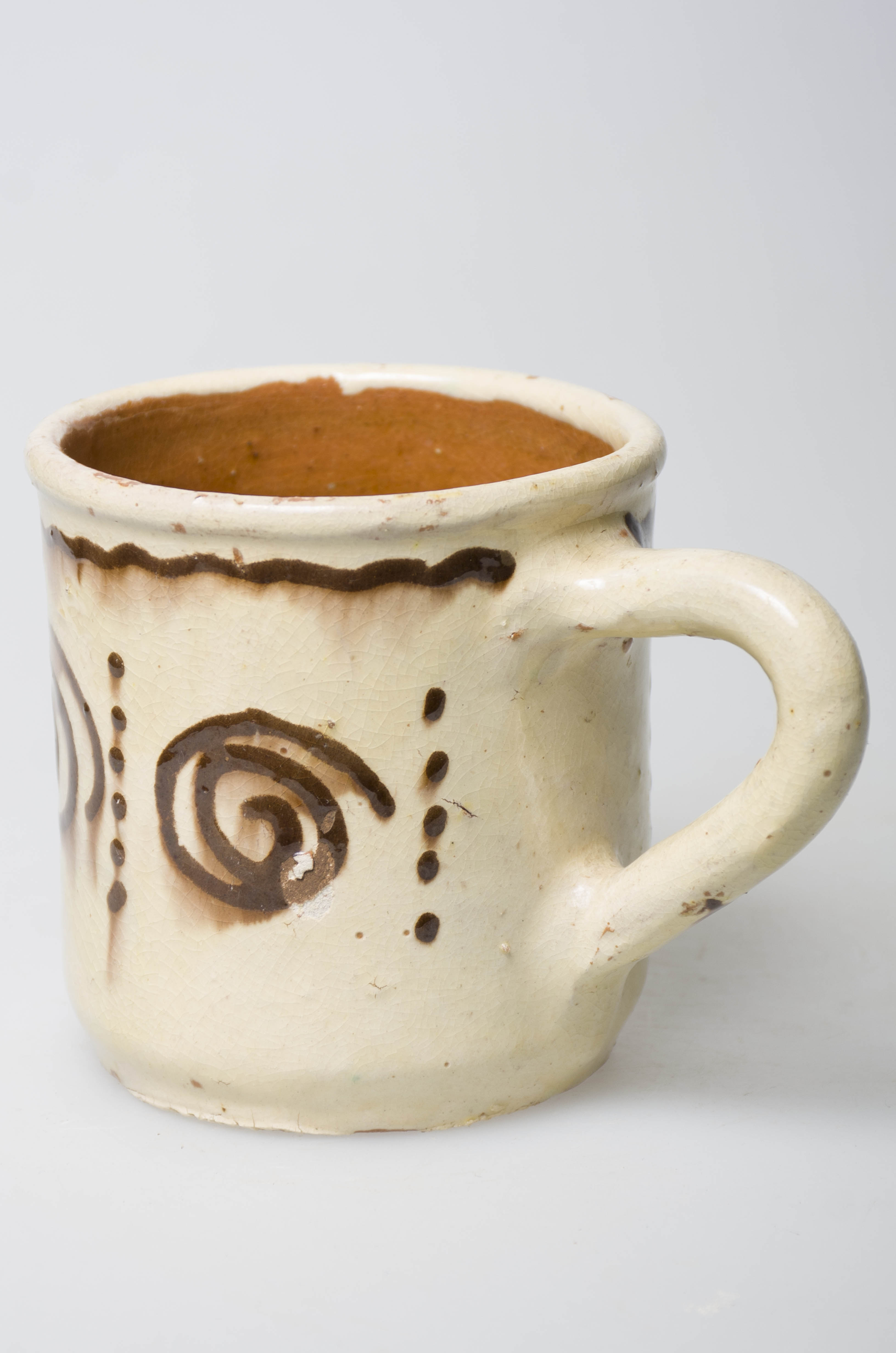 Ceașca este confecționată din ceramică, având forma cilindrică. Aceasta este prevăzută cu o toartă mare. Decorul este pictat: linie ondulată sub buză și patru spirale cu șiruri de puncte verticale dispuse pe corp. Obiectul este smălțuit. Cromatică: fondul este alb, iar motivele sunt pictate cu maro.