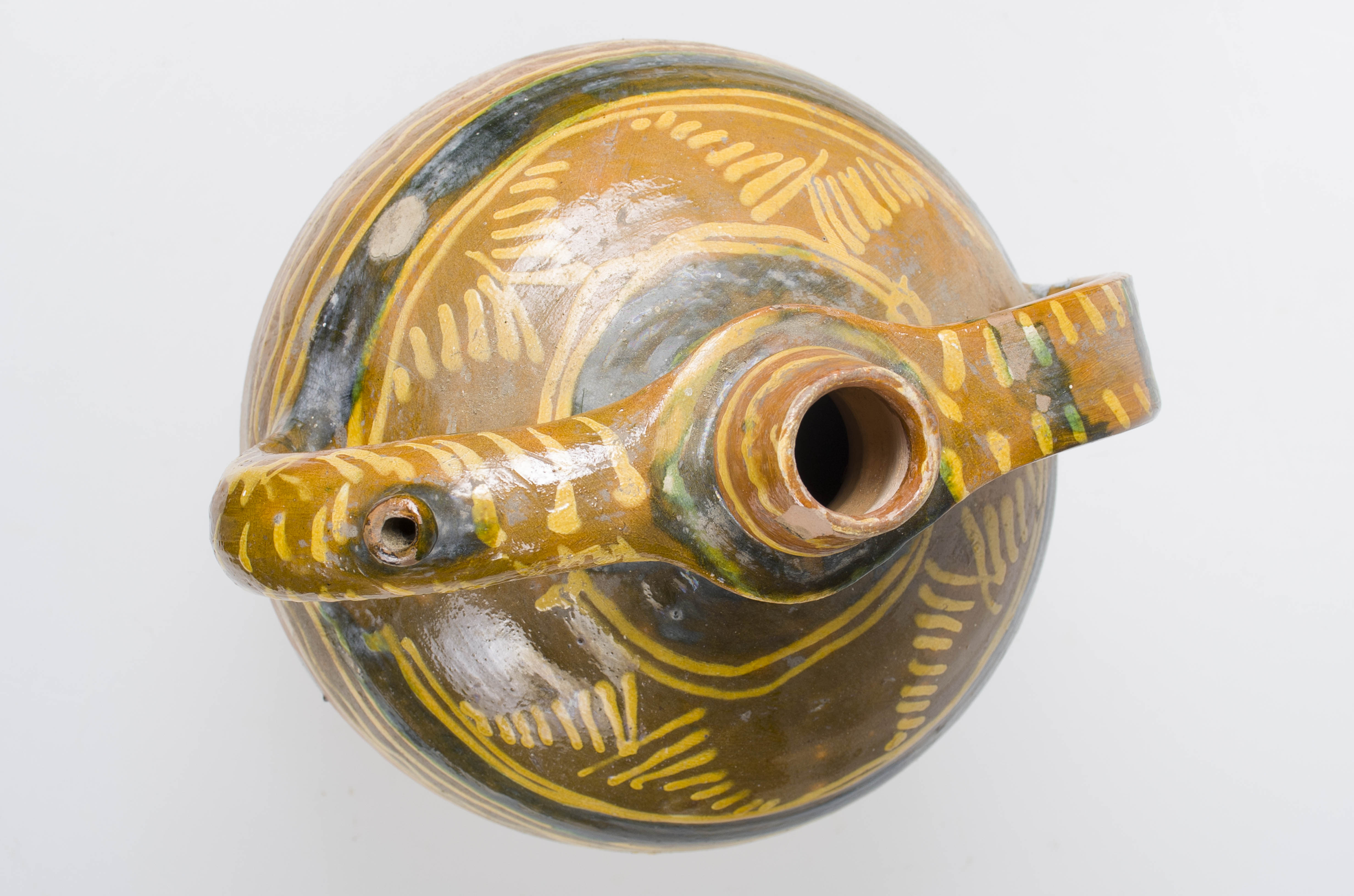 Vas ceramic de formă sferică cu gât îngust. Prezintă două toarte laterale din care una cu ”țâță”. Decorat și smălțuit în jumătatea superioară. Vasul prezintă ornamenteare cu motive geometrice: liniare și curbilinii. Cromatică: crem; stropit cu maro pe partea superioară.
