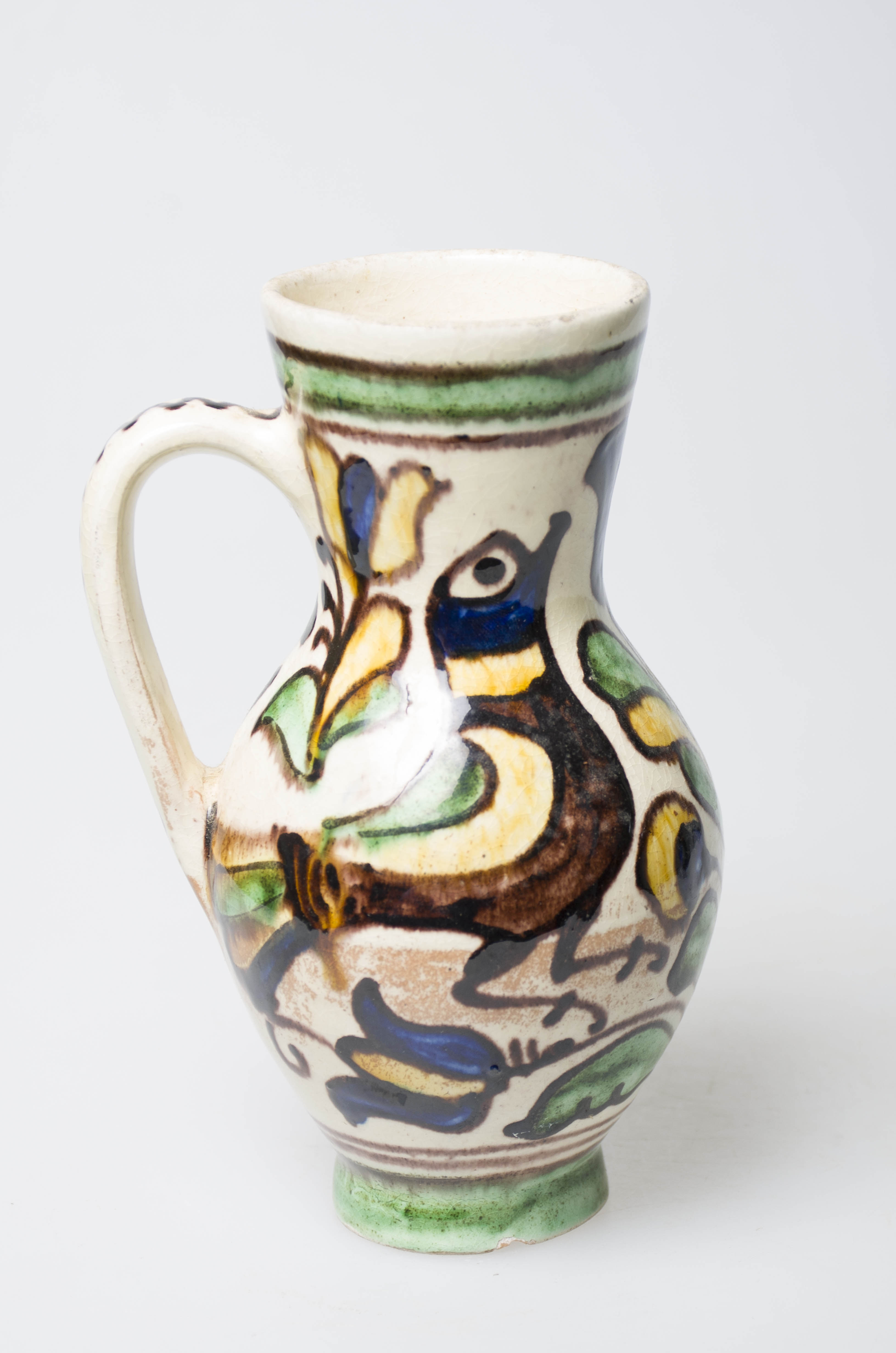Recipient ceramic de formă ovoidală, smălțuit, cu gâtul lung și buza dreaptă. Prevăzut cu o toartă arcuită, care pleacă din mijlocul gâtului spre partea inferioară a vasului. Intens stilizat cu motive avimorfe (două păsări cu penaj diferit disupse față în față), florale și vegetale (lalele, bulbi, crengi și frunze) pictate multicolor cu pensula, cu smalț. Decorarea este delimitată de linii circulare de diferite grosimi, dispuse la extremitățile vasului. Avem un motiv geometric pe toartă sub formă de linie meandrică. Cromatică: fundal: crem; motive: galben; albastru; verde; maro.
